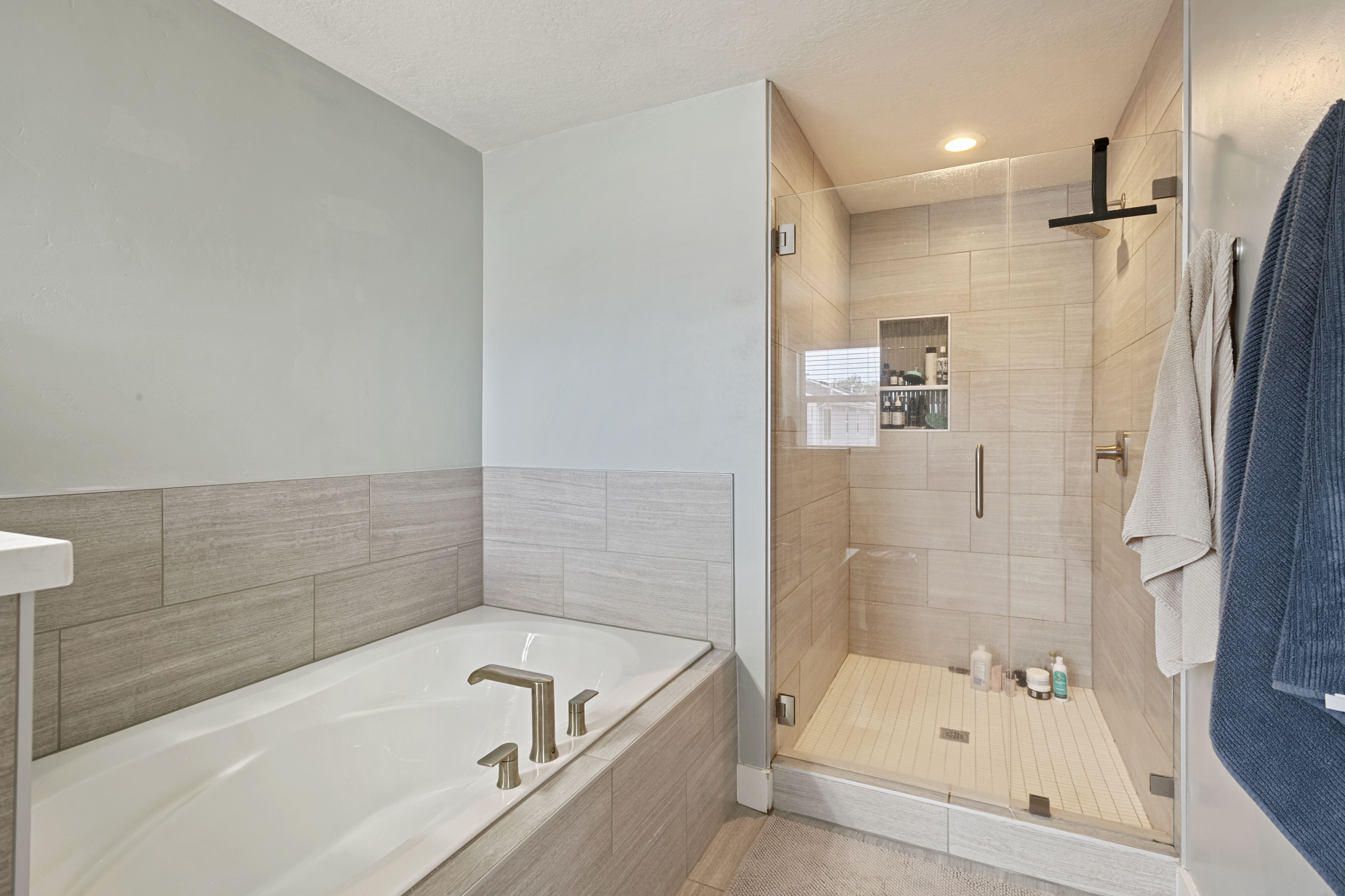 Modern bathroom featuring a soaking tub with brushed nickel fixtures, a glass-enclosed shower with a built-in niche, and large format wall tiling