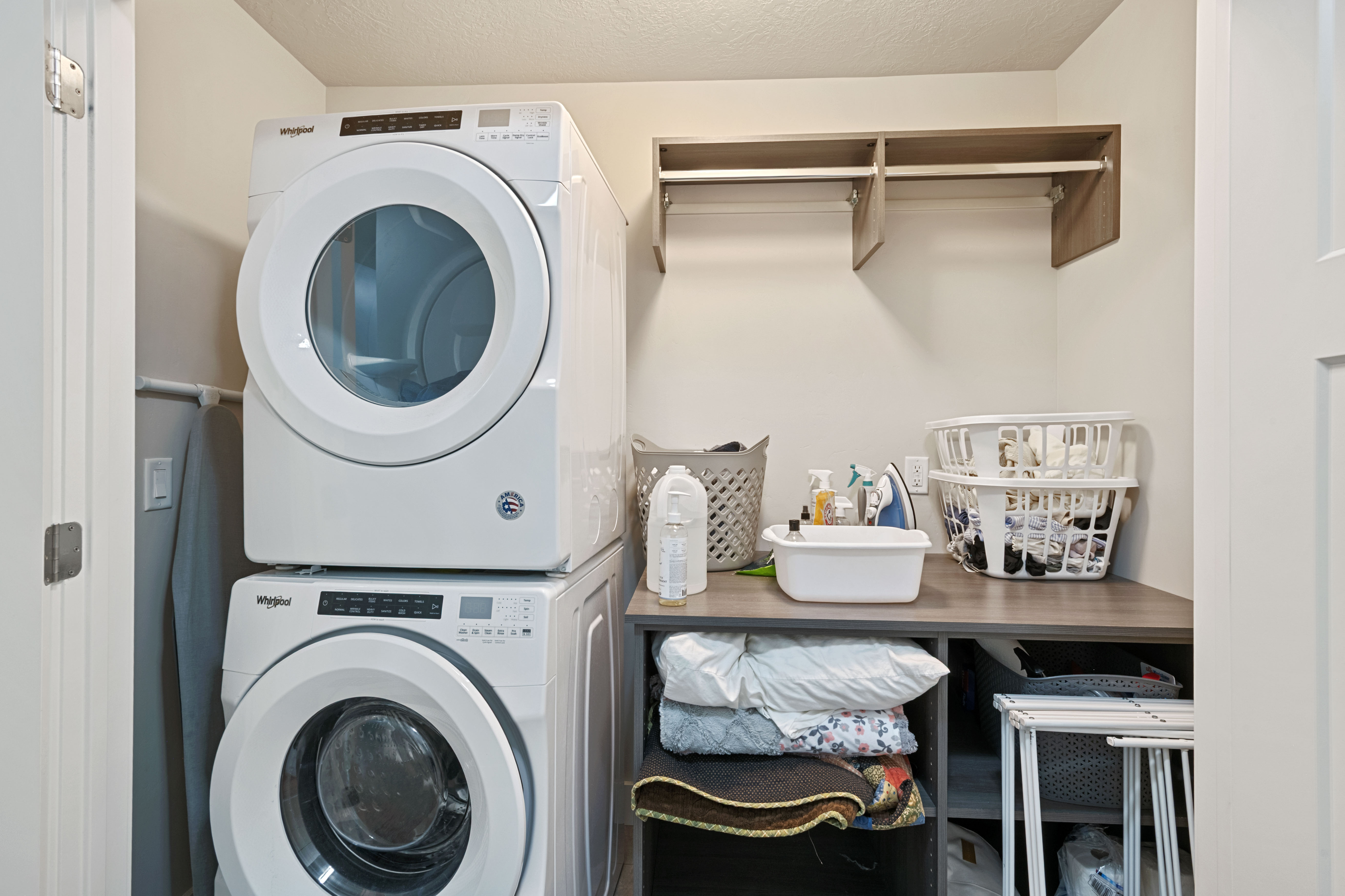 Dedicated laundry area featuring a stacked washer and dryer, a wood-finish countertop, and built-in shelving with a hanging rod