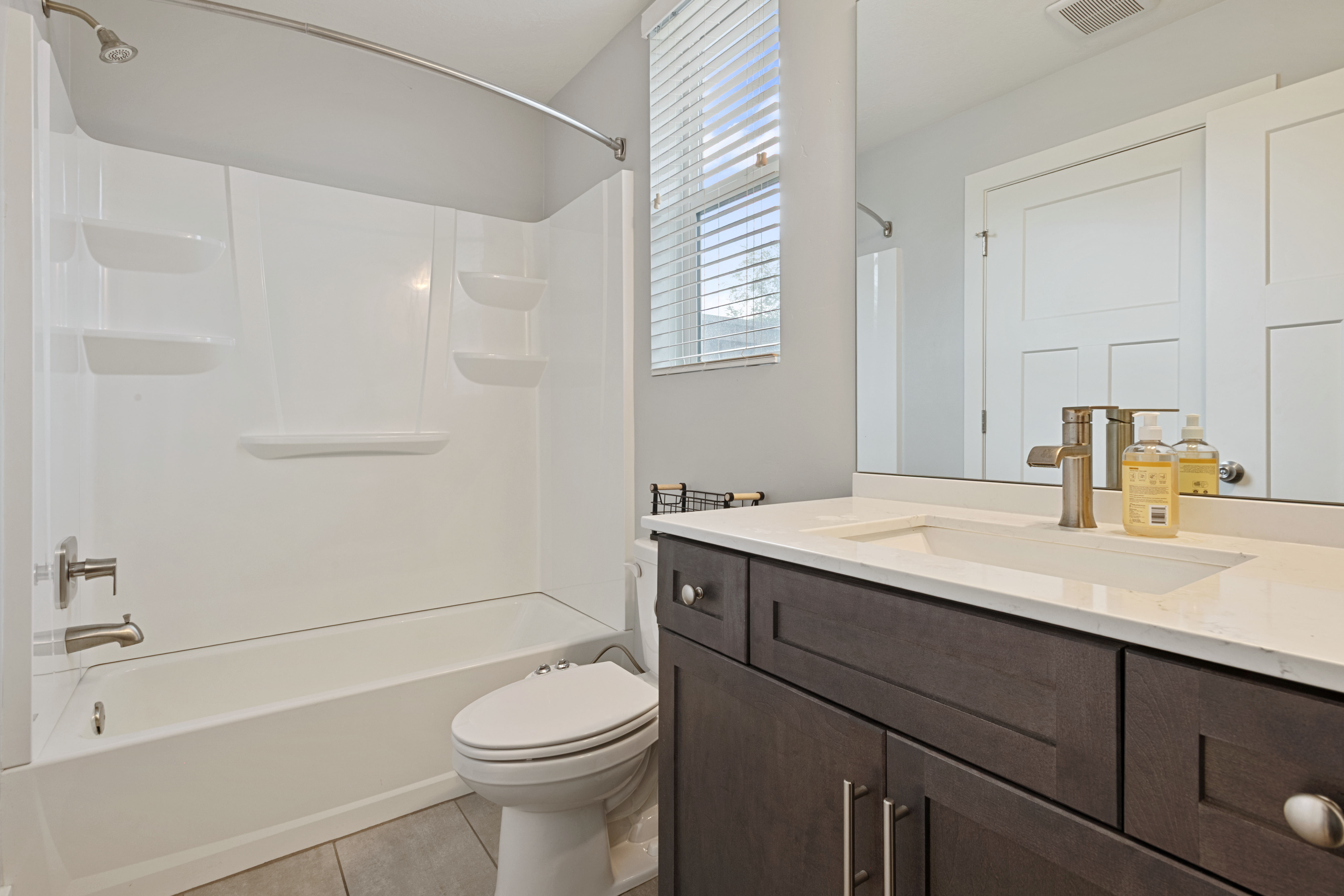 Bathroom featuring a white tub/shower combination, dark wood-finish vanity with an integrated sink, quartz-finish countertop, and brushed nickel fixtures