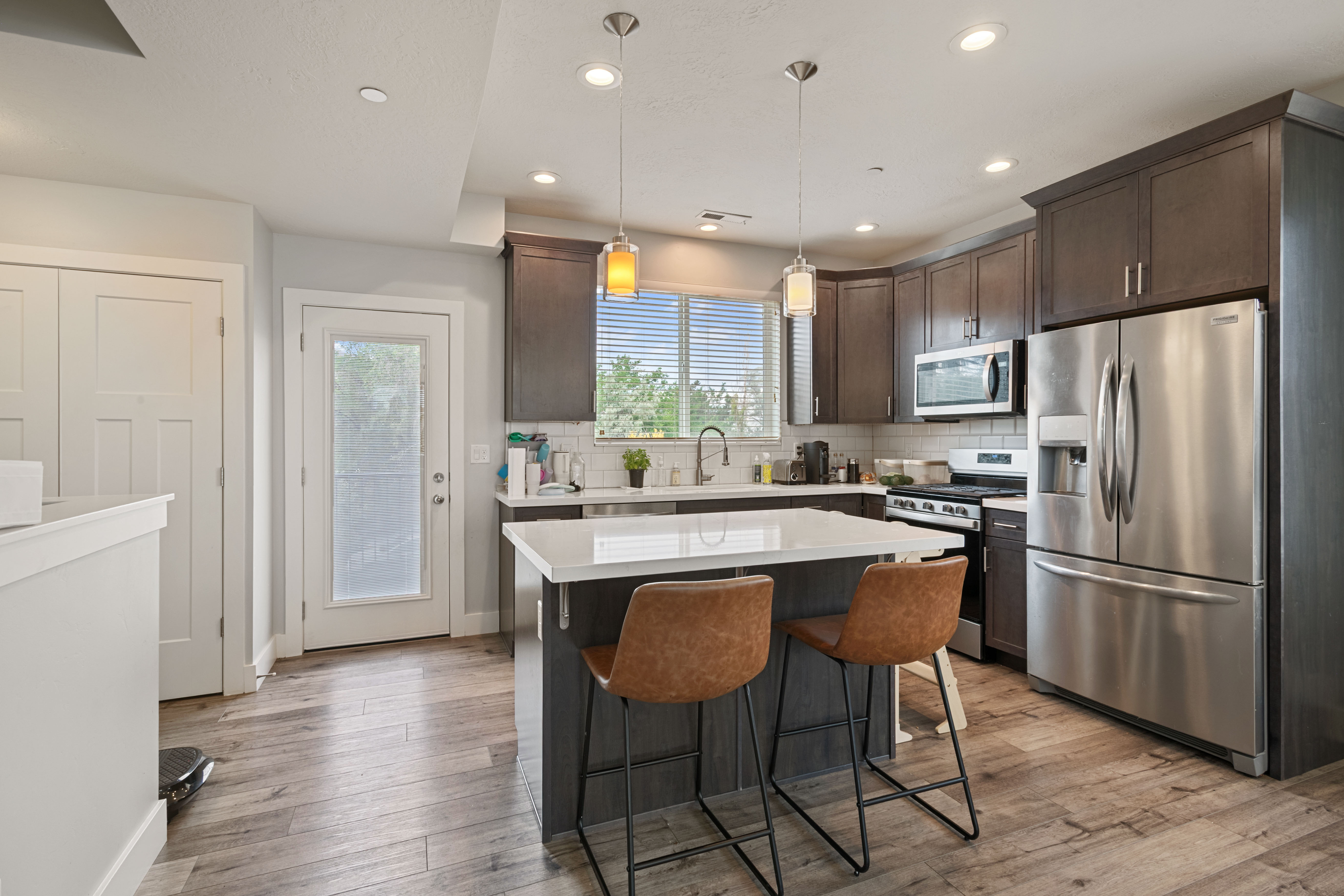 Contemporary kitchen featuring dark wood cabinetry, stainless steel appliances, and a central island with a white countertop