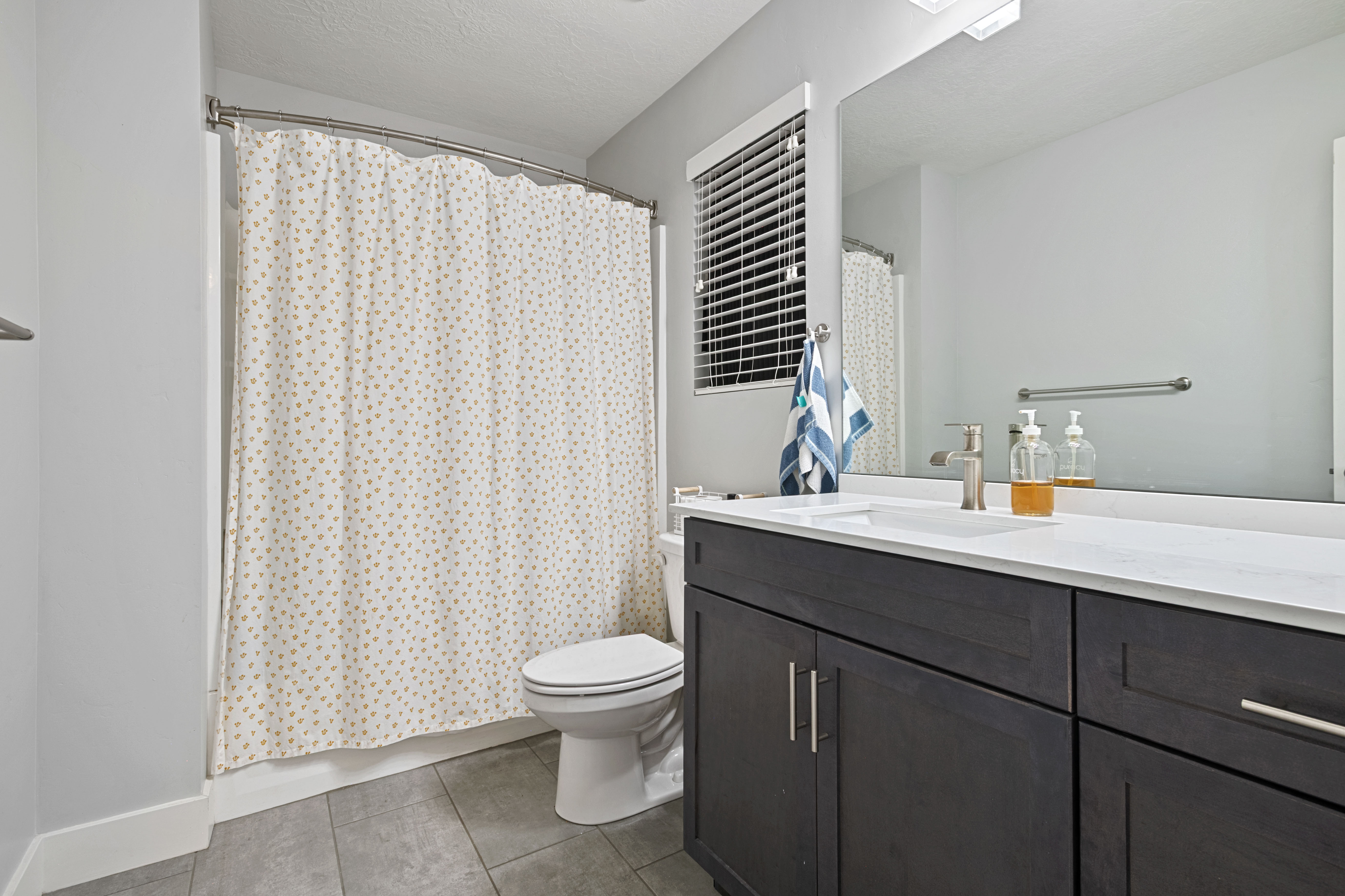 Bathroom featuring a dark wood-finish vanity with a white countertop and undermount sink, a large wall-mounted mirror, and tile flooring
