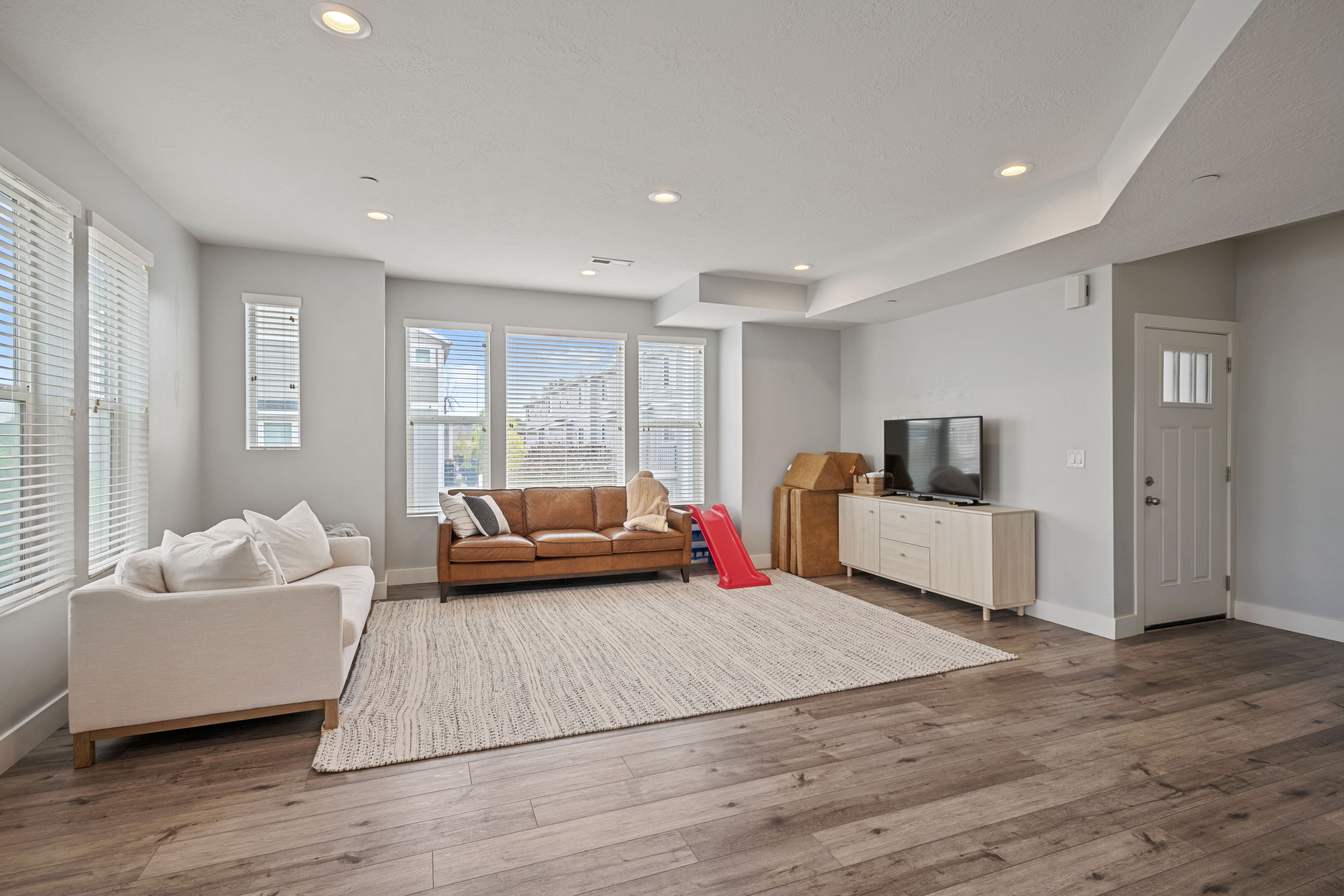 Spacious living area featuring extensive wood-finish flooring, recessed lighting, and multiple windows with blinds