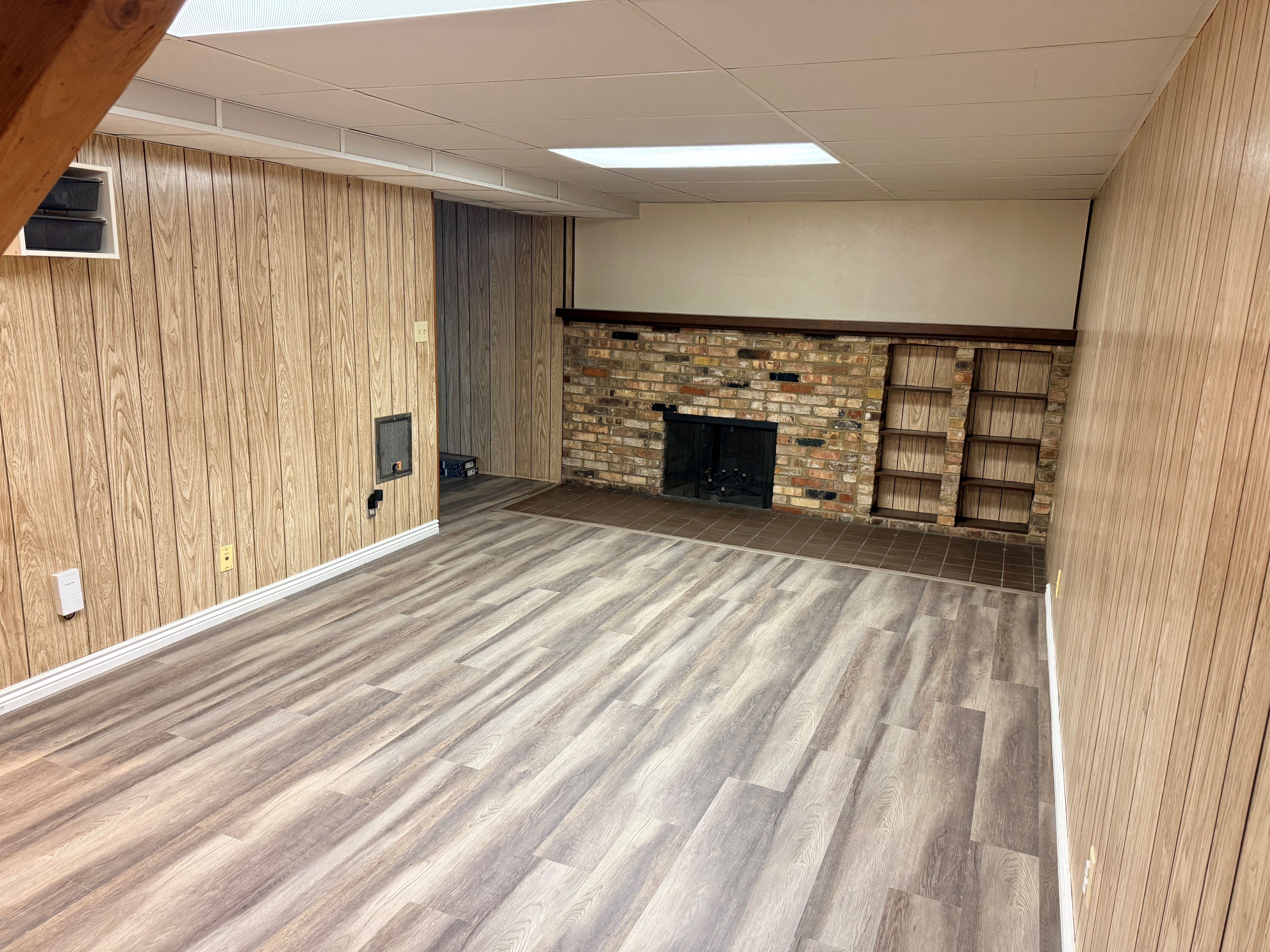 Spacious room featuring wood-finish wall paneling and light wood-finish flooring