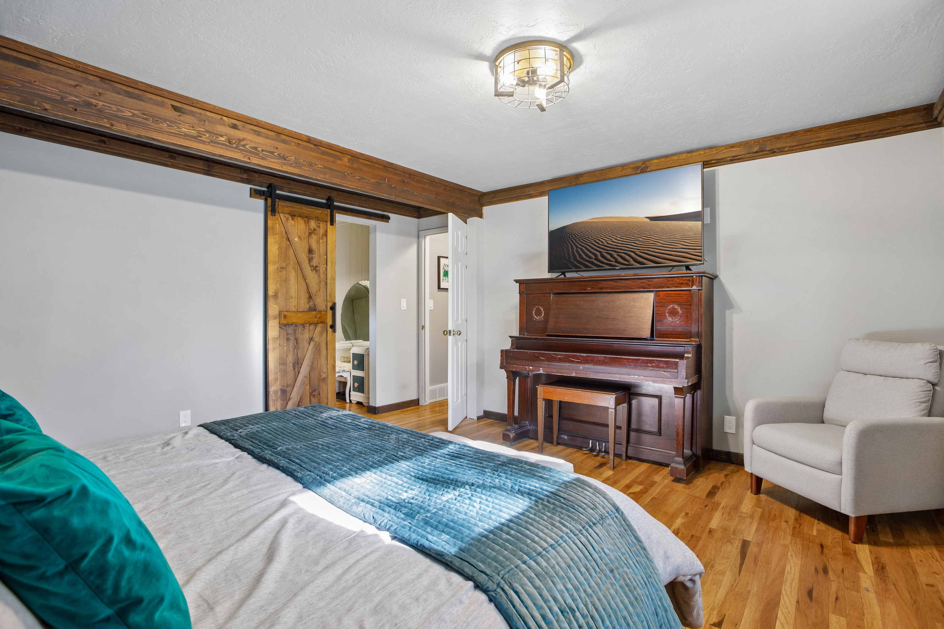 Spacious interior featuring wood-finish flooring, exposed ceiling beams, a decorative ceiling light fixture, light gray wall paint, and a rustic wood barn door