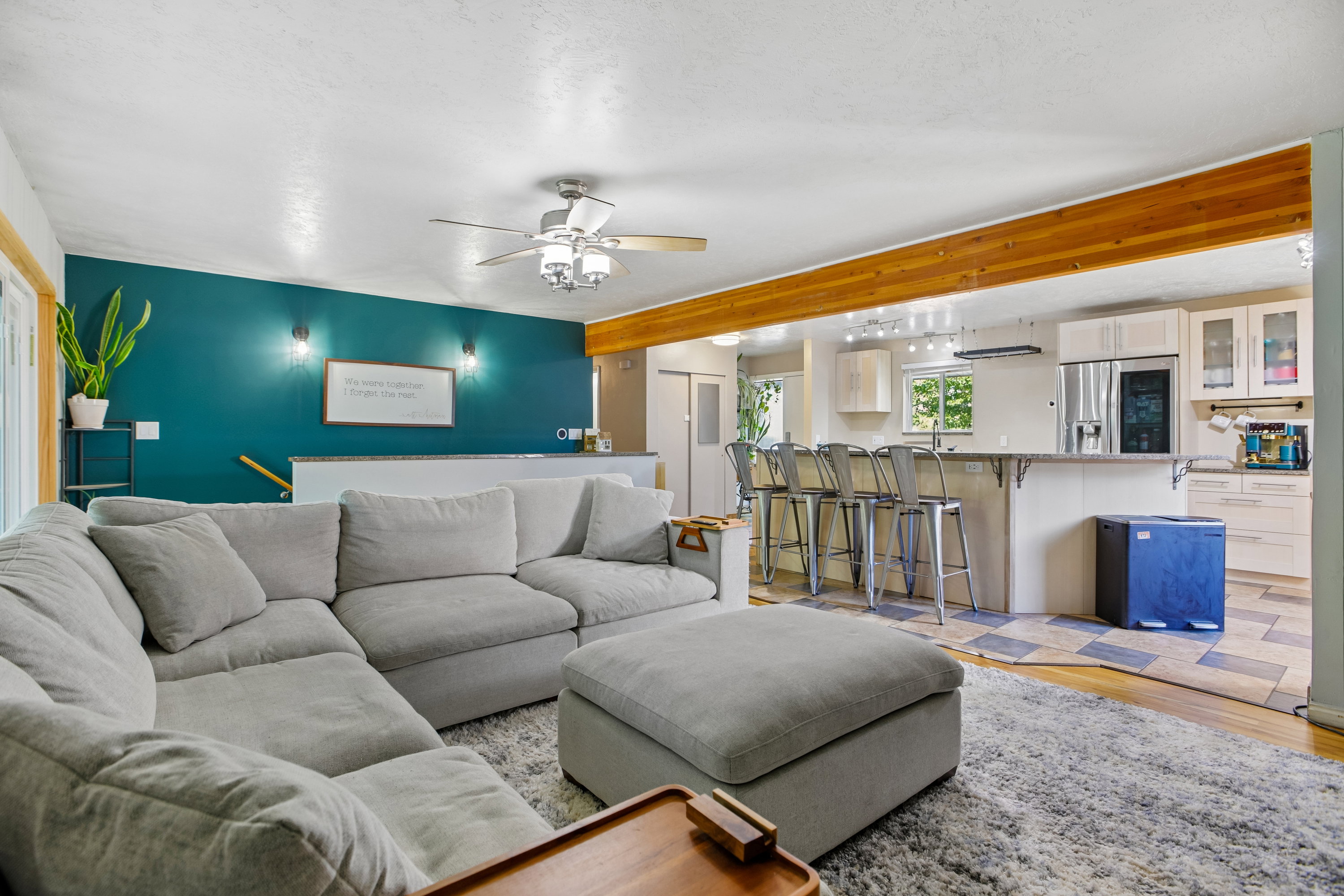 Spacious open-concept living area featuring a vibrant accent wall, wood-finish flooring, a ceiling fan, and exposed wood beam accents