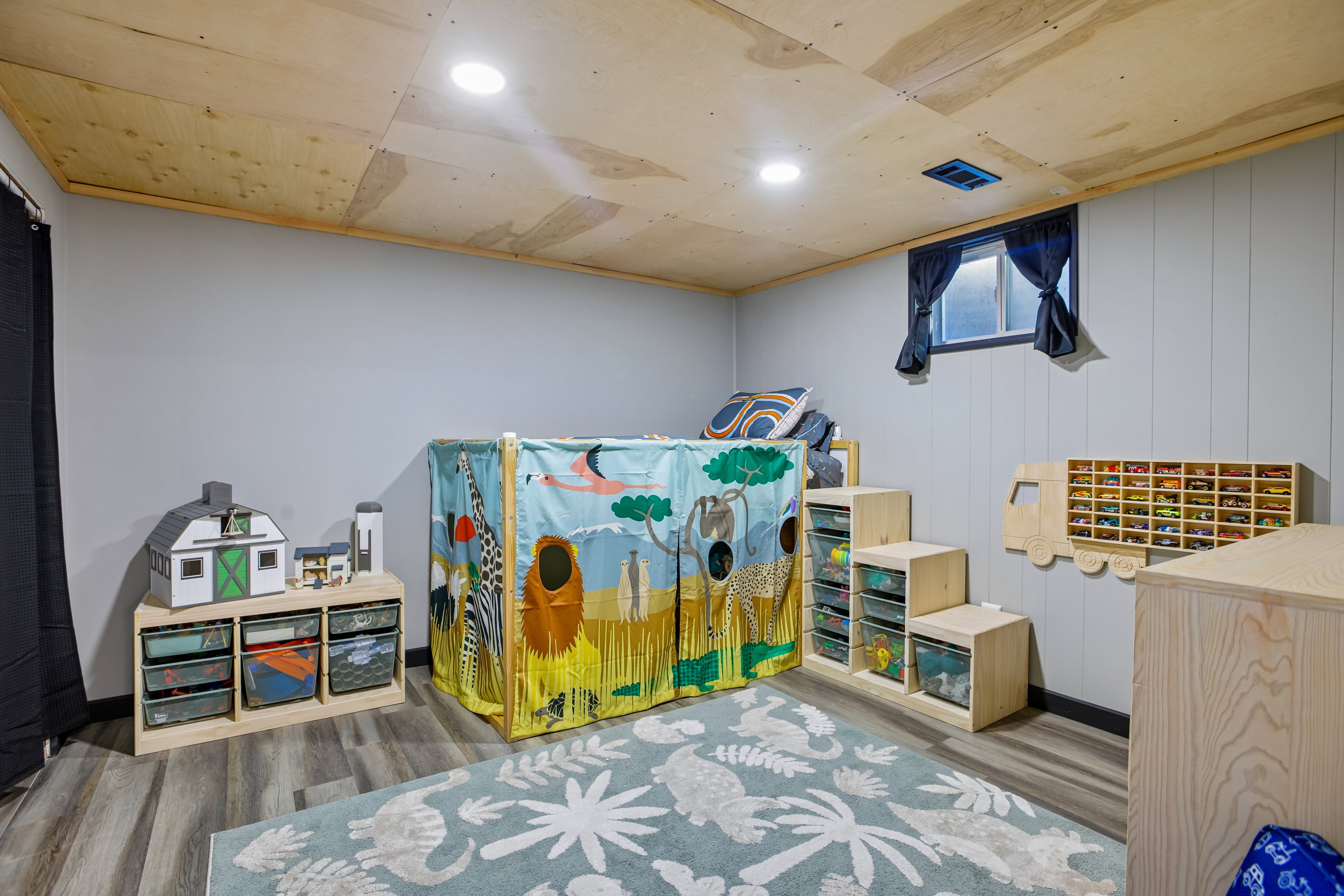 Recessed lighting illuminates a room with wood-finish flooring and light gray paneled walls
