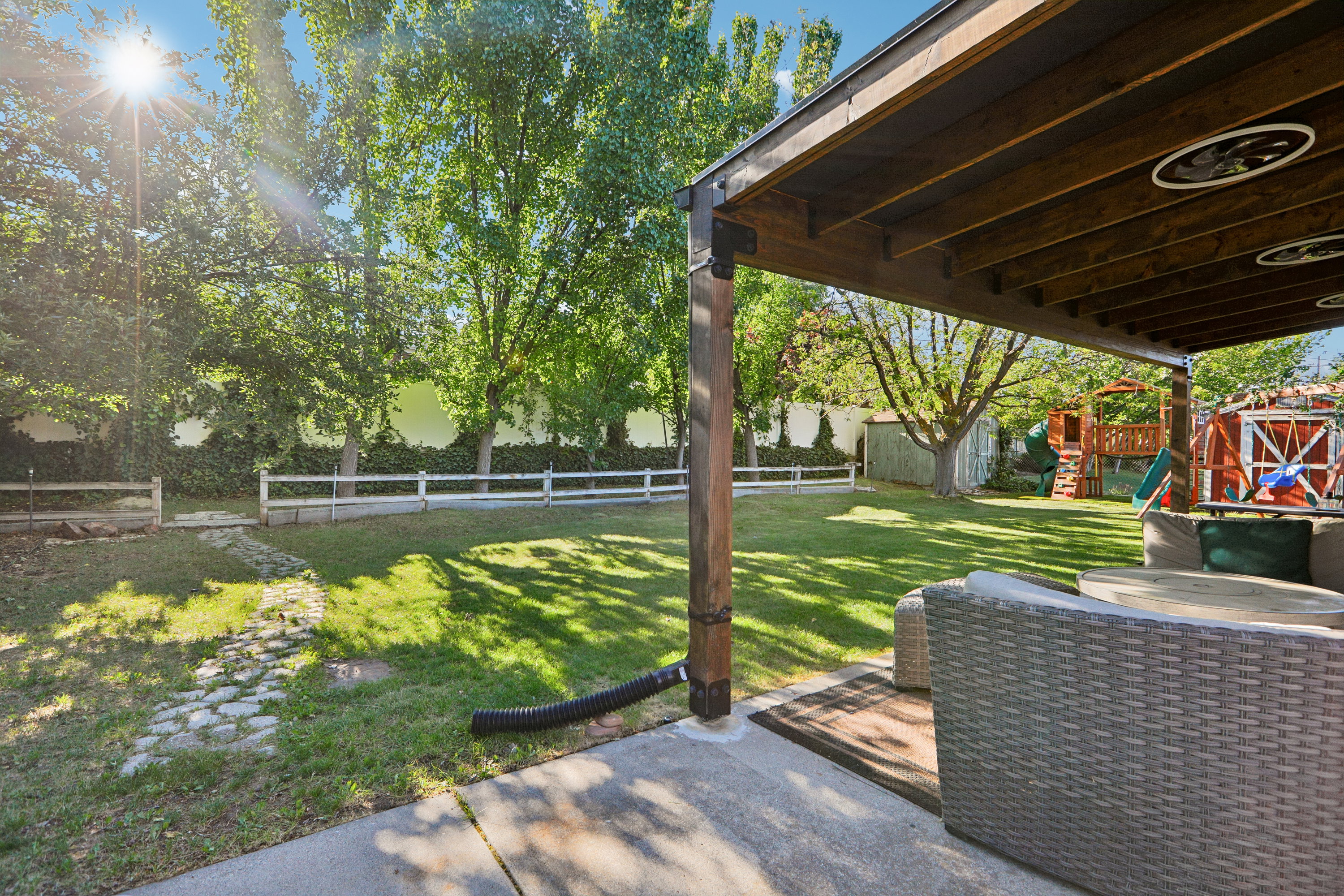 Covered patio with recessed lighting overlooking a spacious lawn, mature trees, and a white split-rail fence