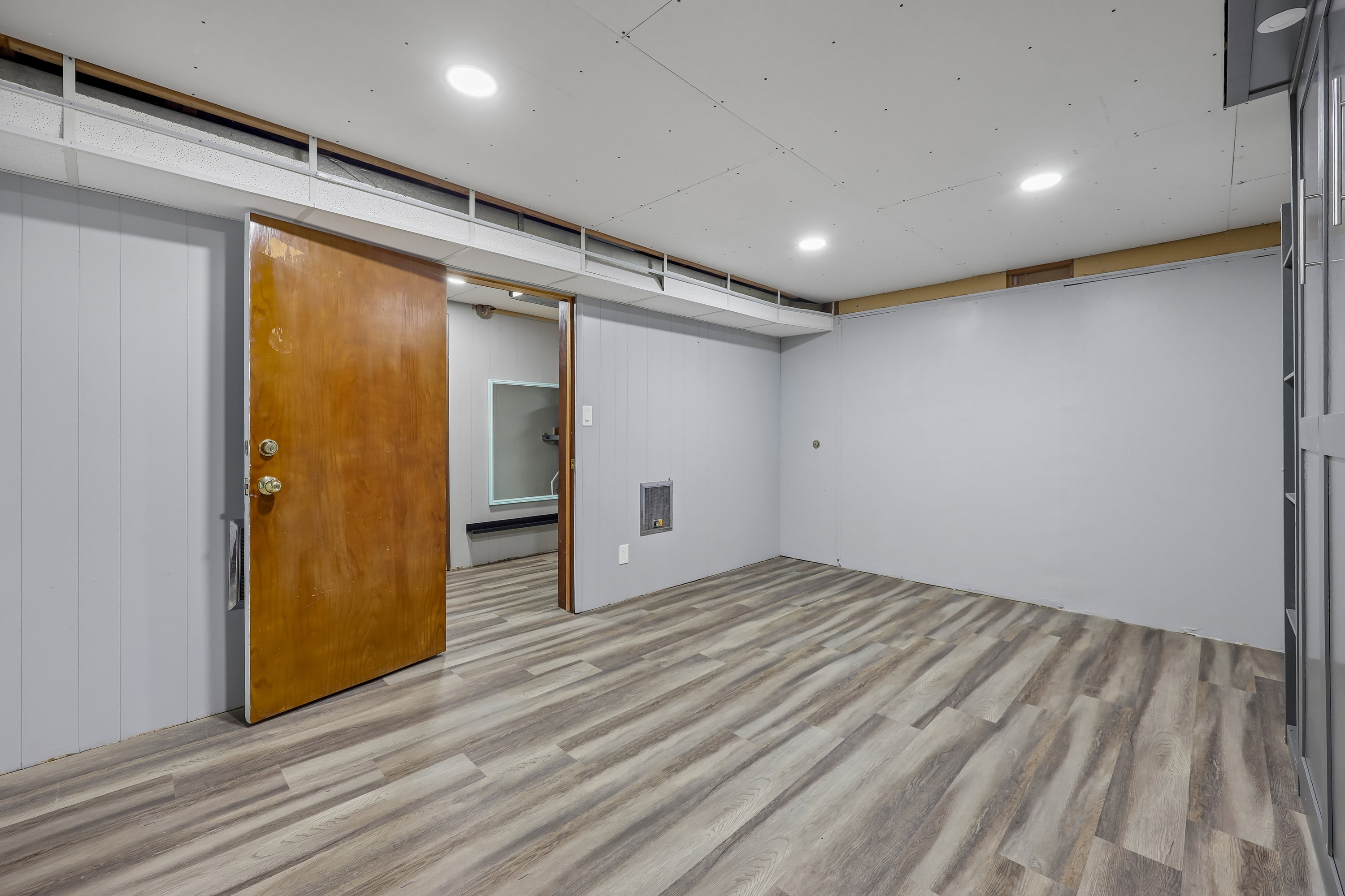 Spacious room featuring wood-finish flooring, recessed lighting, light gray paneled walls, and a wood door