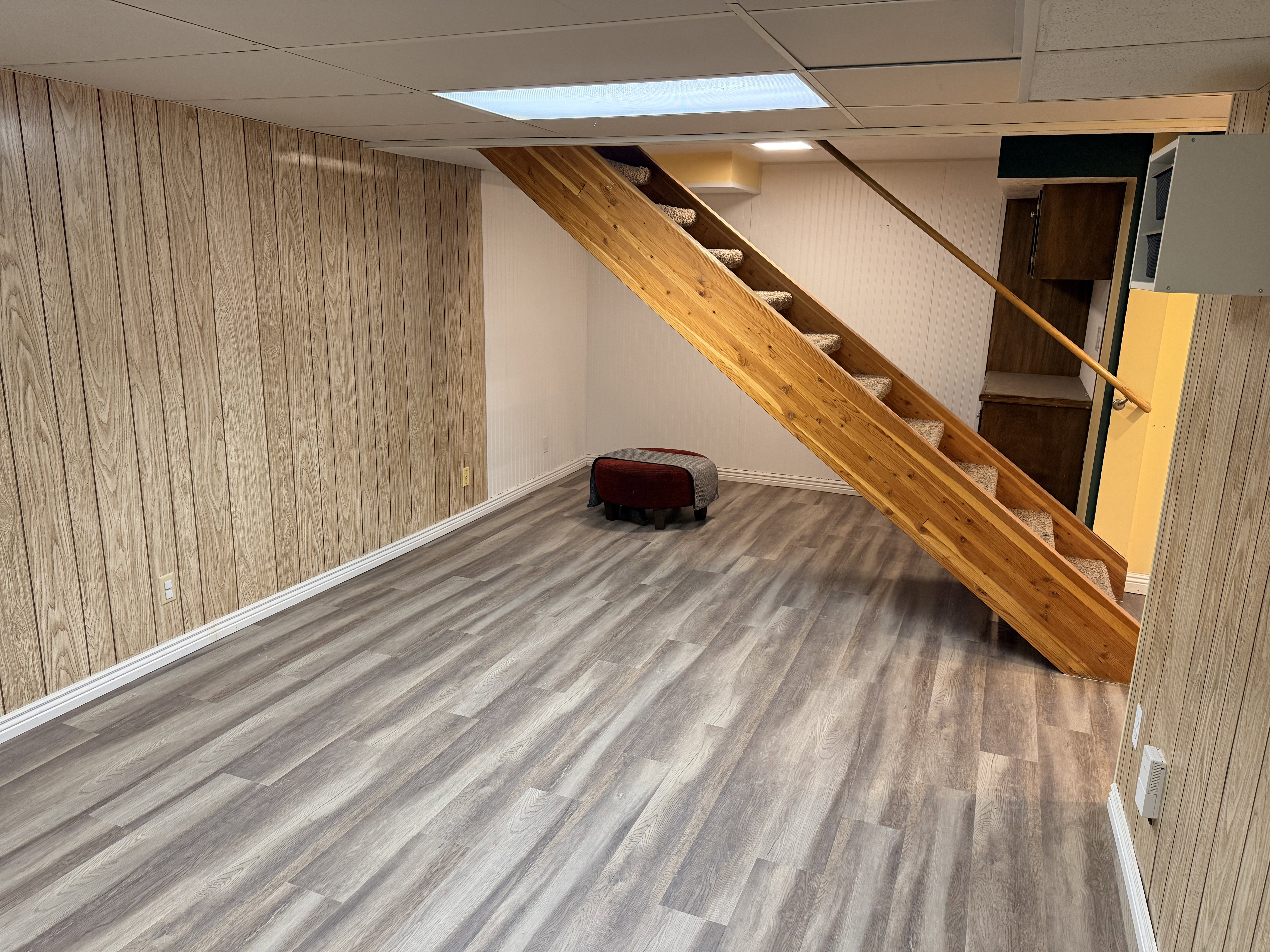 Spacious room with wood-finish paneling, contemporary wood-finish flooring, and a prominent wooden staircase with carpeted treads