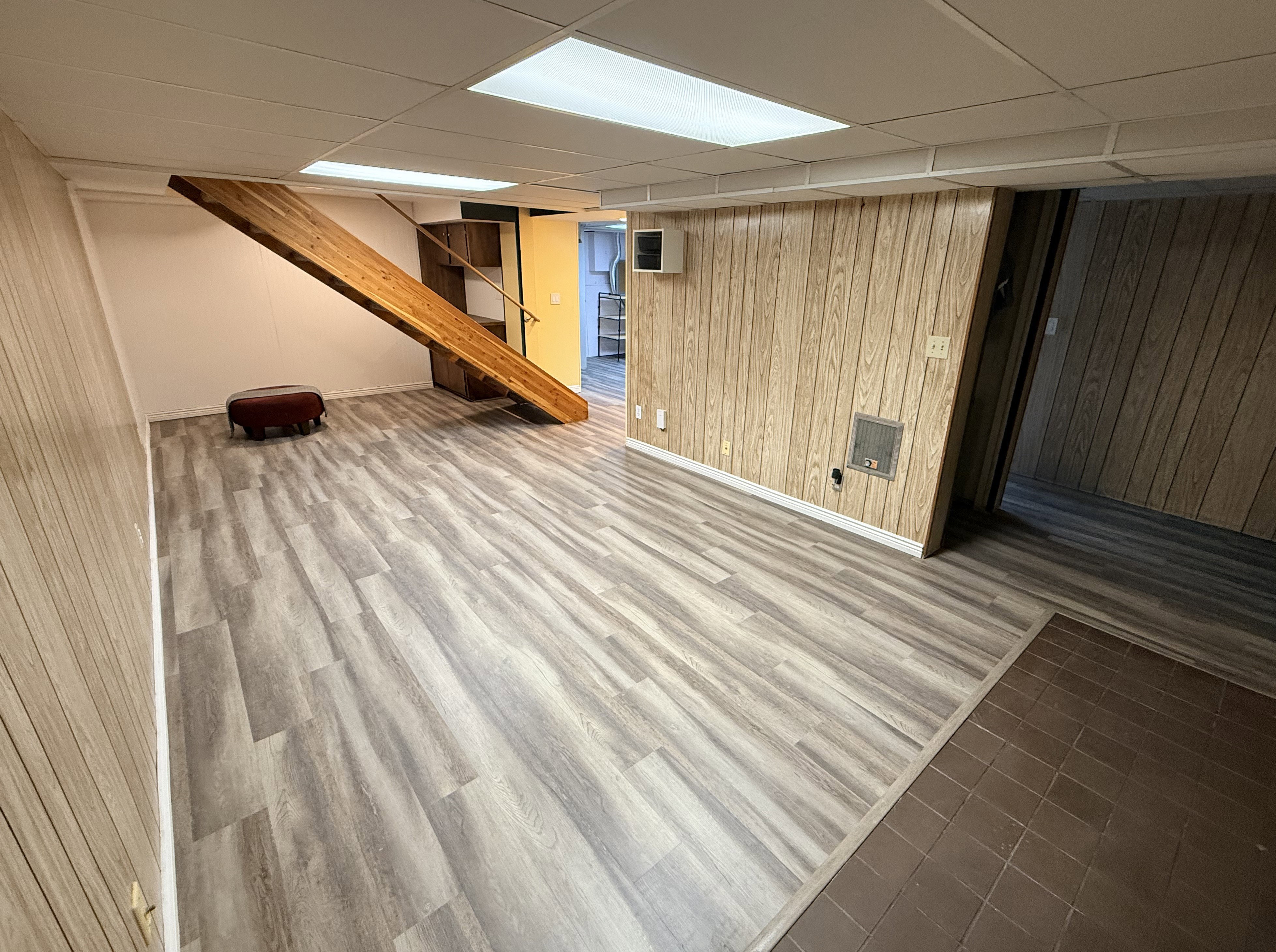 Spacious lower-level area with wood-finish flooring, wood paneling, and an exposed wood staircase