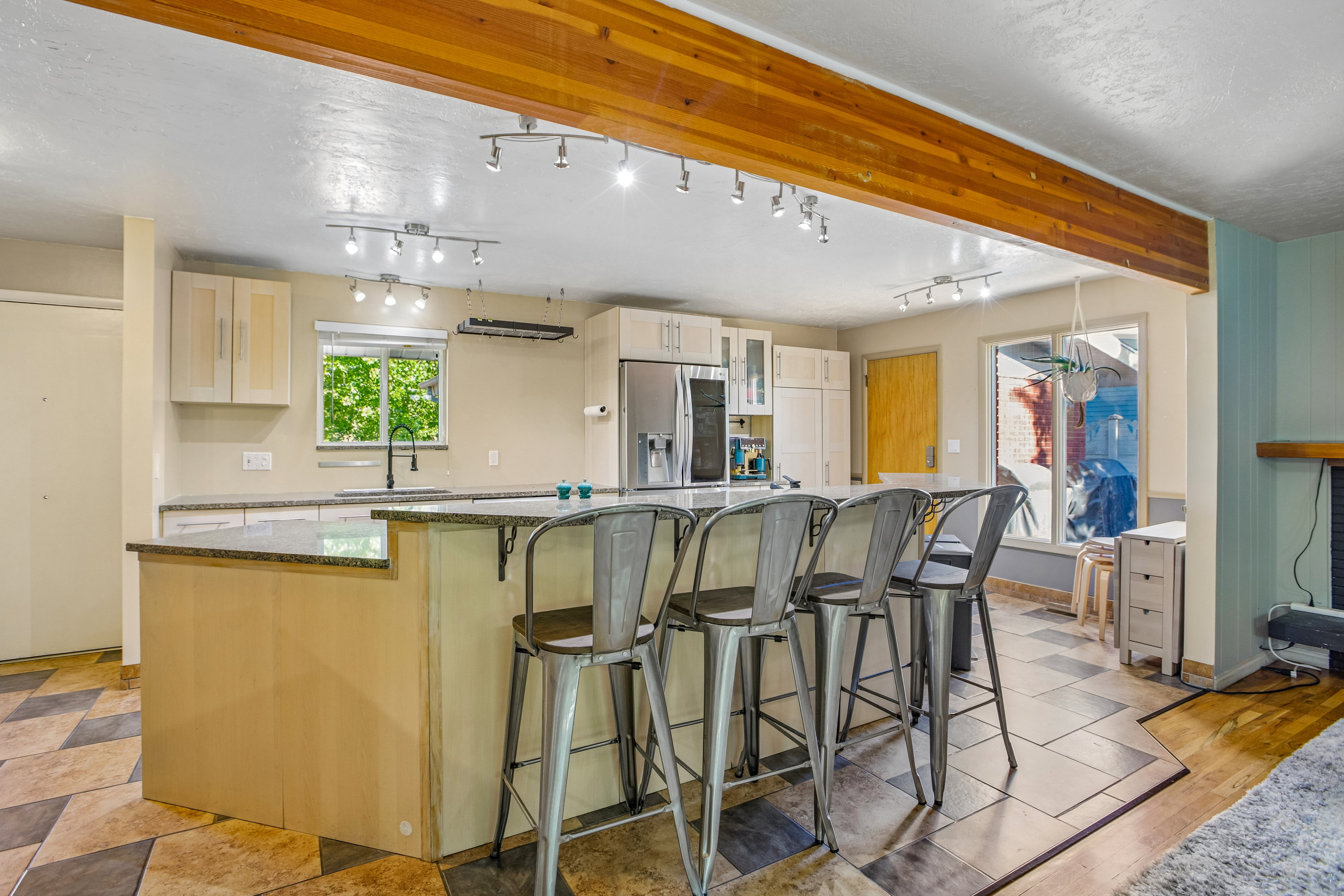Spacious kitchen featuring a large island with seating, a stainless steel refrigerator, light-toned cabinetry, and granite countertops