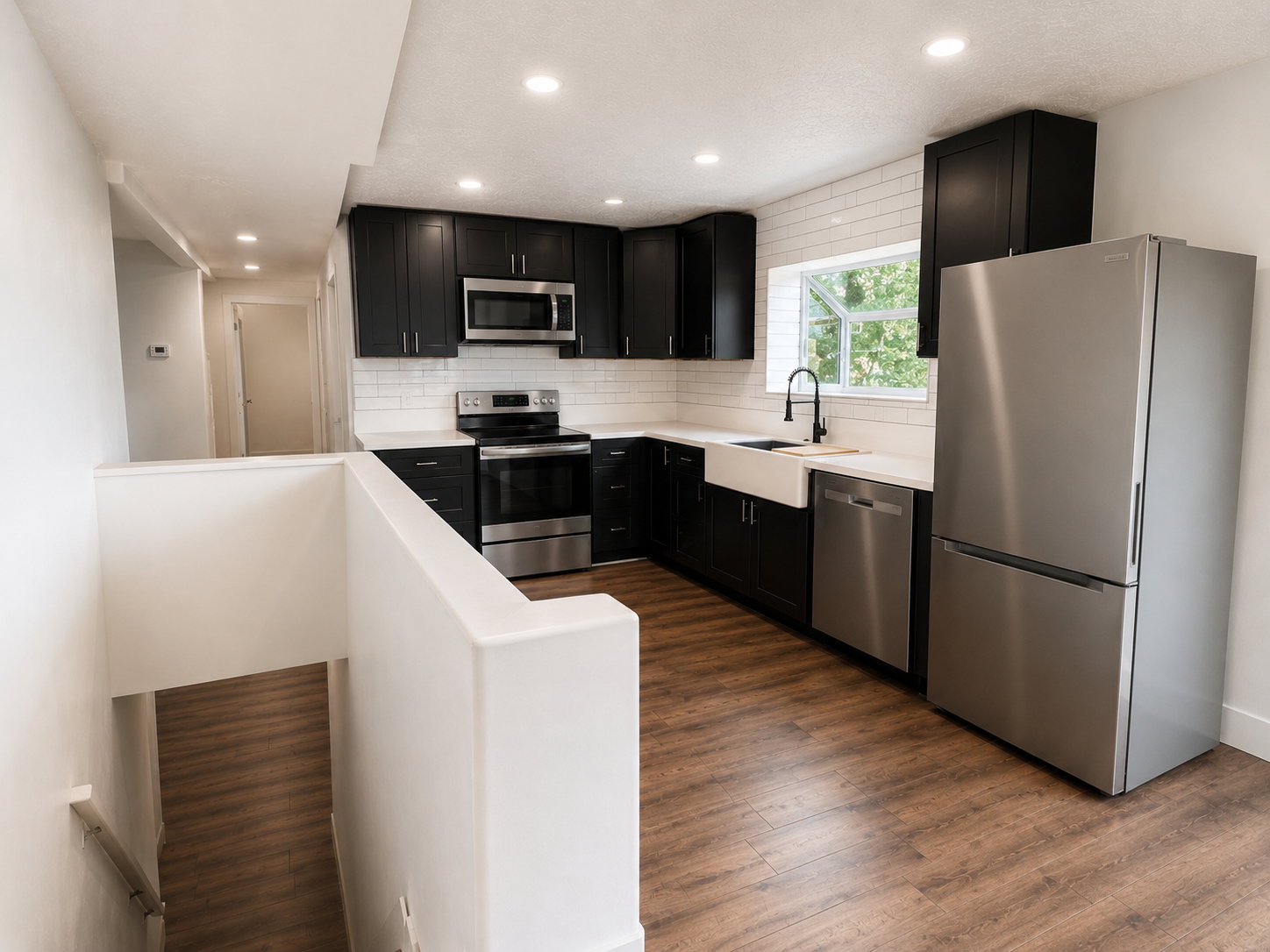 Modern kitchen featuring dark cabinetry, stainless steel appliances, white subway tile backsplash, a farmhouse sink, and wood-finish flooring