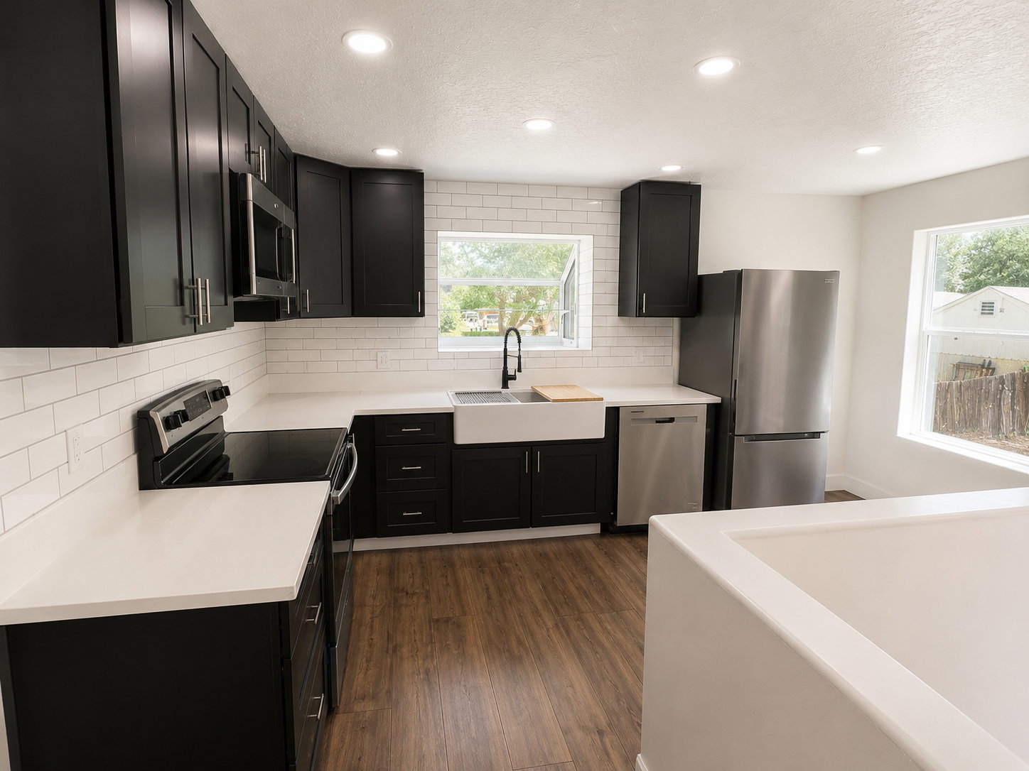 Modern kitchen featuring dark cabinetry with brushed nickel hardware, white subway tile backsplash, and light-colored countertops