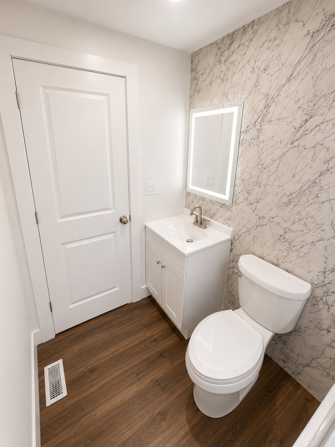 Bathroom featuring a white vanity with an integrated sink, illuminated mirror, wood-finish flooring, and a patterned accent wall
