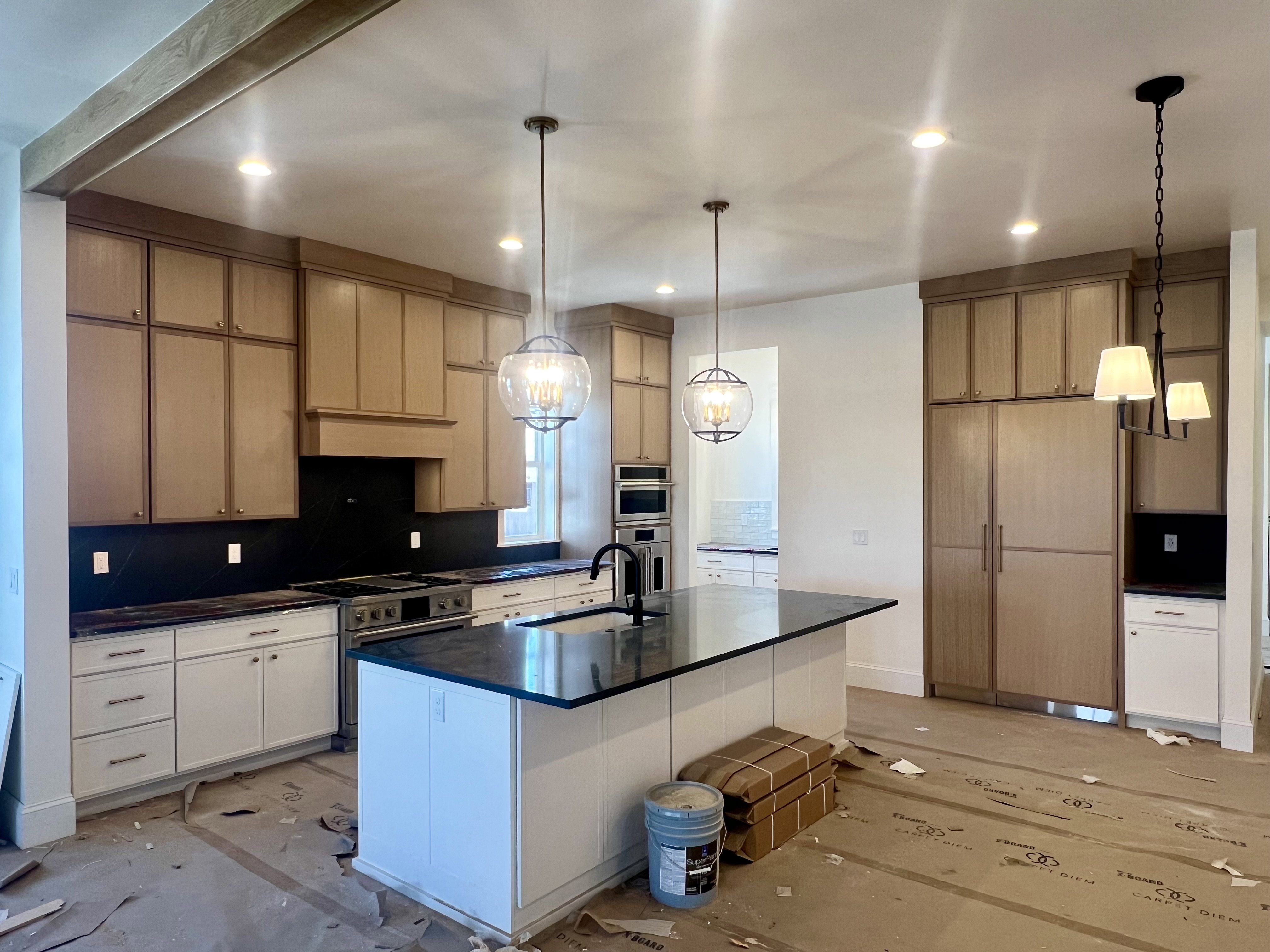 Kitchen featuring a large island with black countertop, full-height light wood-finish cabinetry, white base cabinetry, stainless steel appliances, and recessed lighting