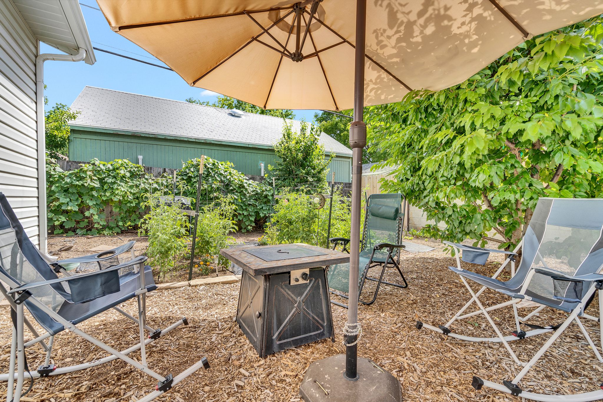 Backyard patio area featuring wood chip ground cover, mature landscaping, and an adjacent building with horizontal siding