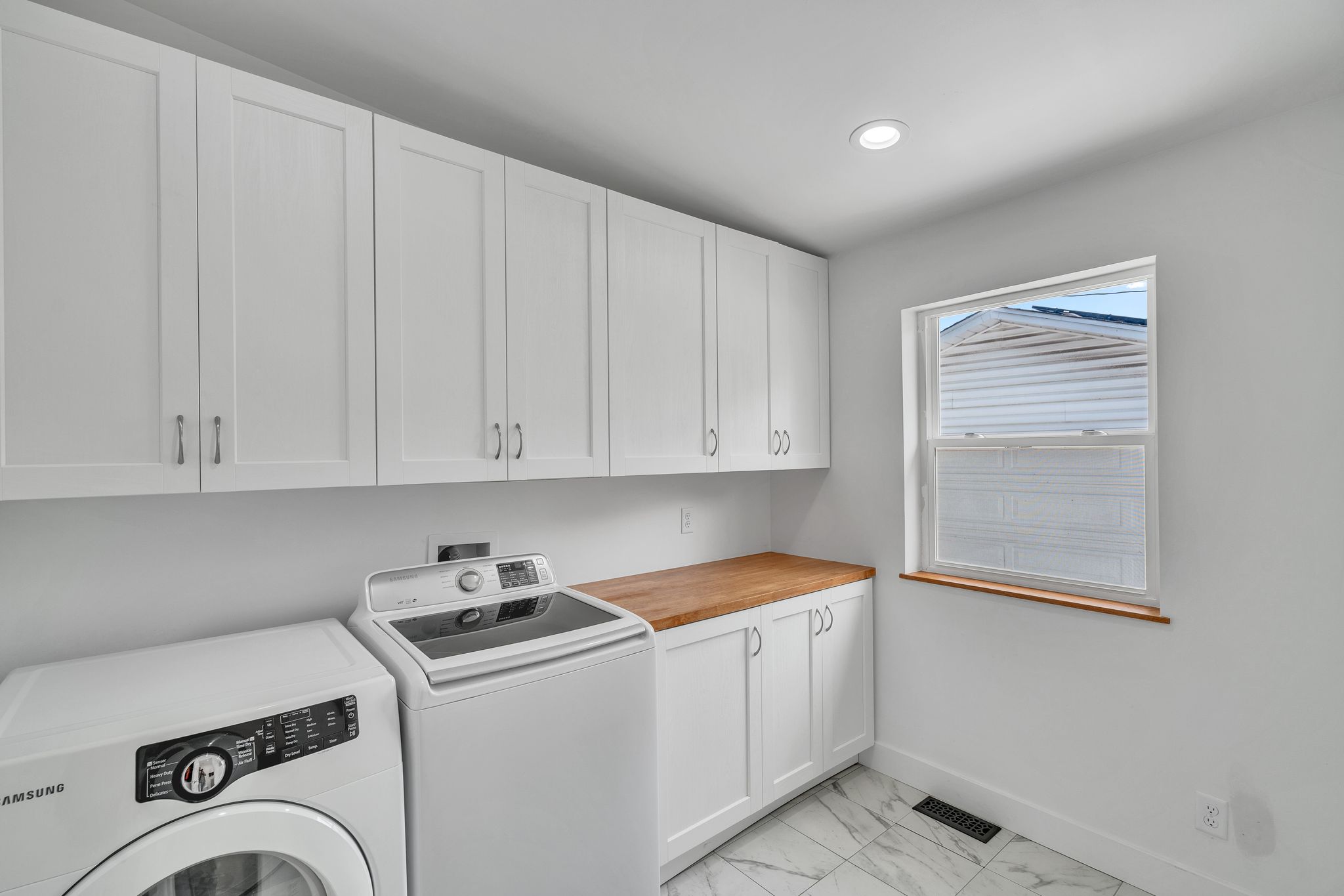 Laundry room featuring white shaker cabinetry, wood-finish countertop, and a window with wood trim
