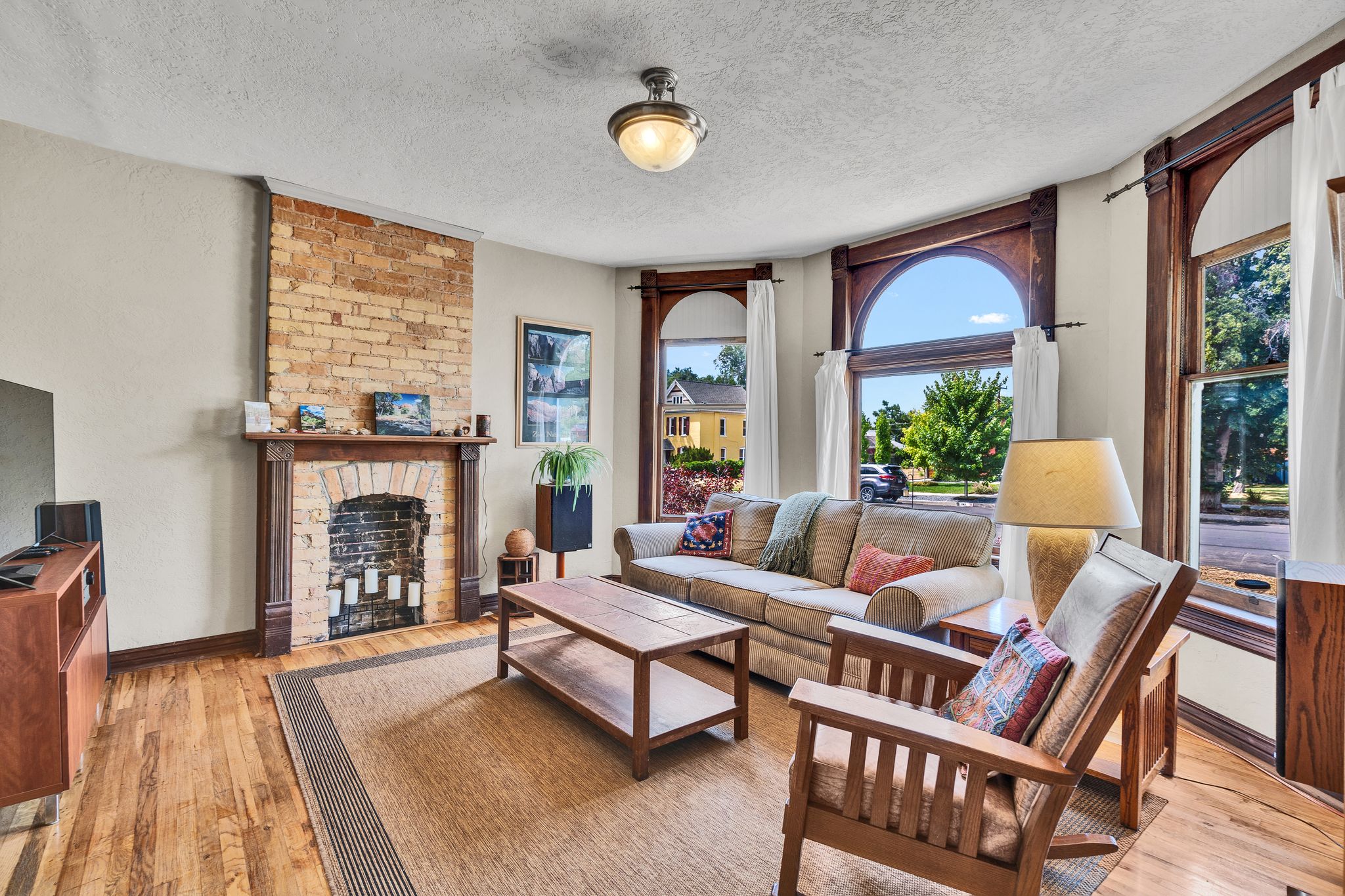 Living area featuring exposed brick fireplace, hardwood flooring, and bay windows