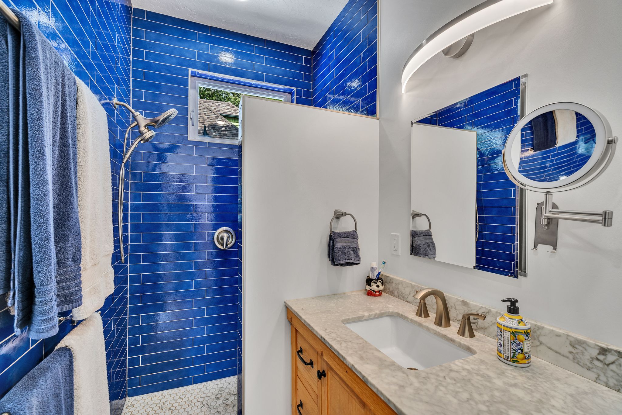 blue subway tile surround and a window, complemented by a vanity with a light-colored countertop