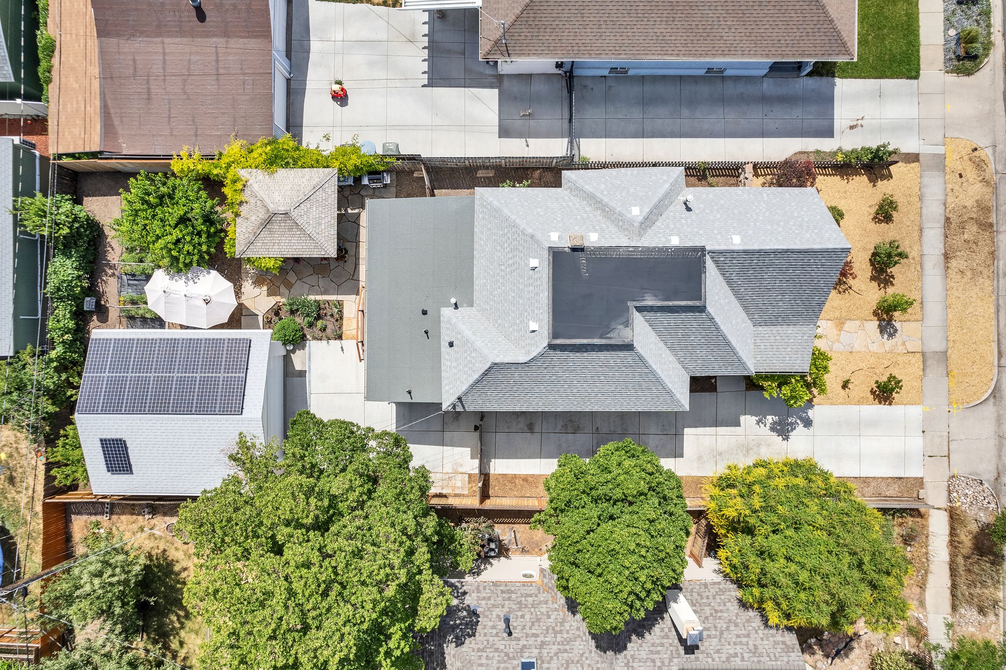 Aerial perspective showcasing a property with a grey shingled roof, a separate structure featuring solar panels, and extensive concrete paving