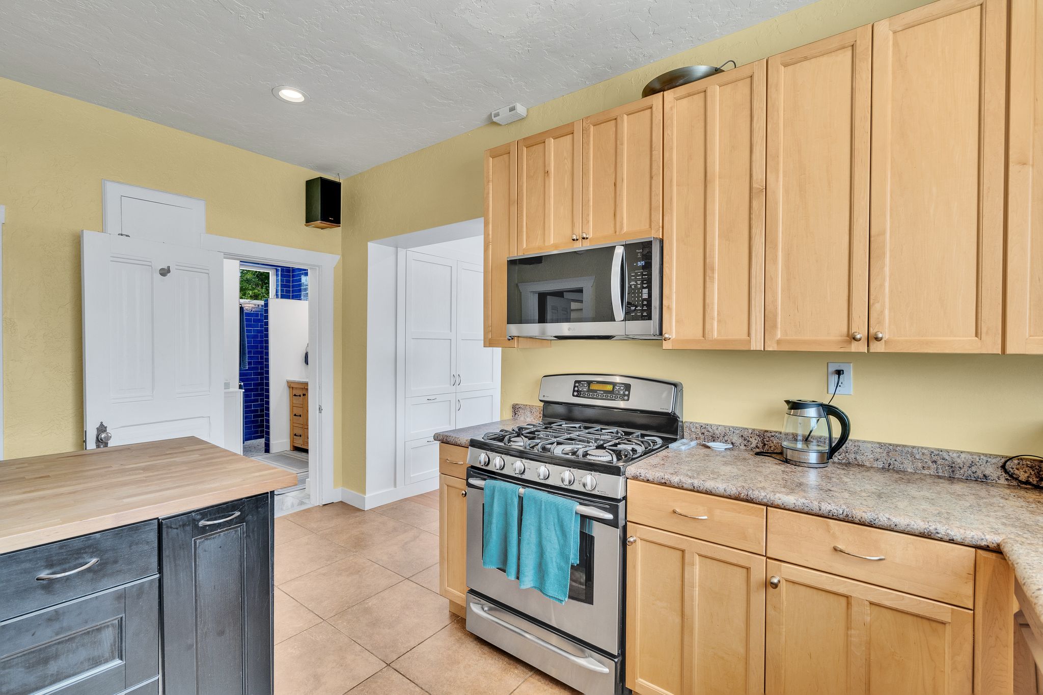 Kitchen featuring a stainless steel gas range, microwave, light wood-finish cabinetry, and patterned countertops