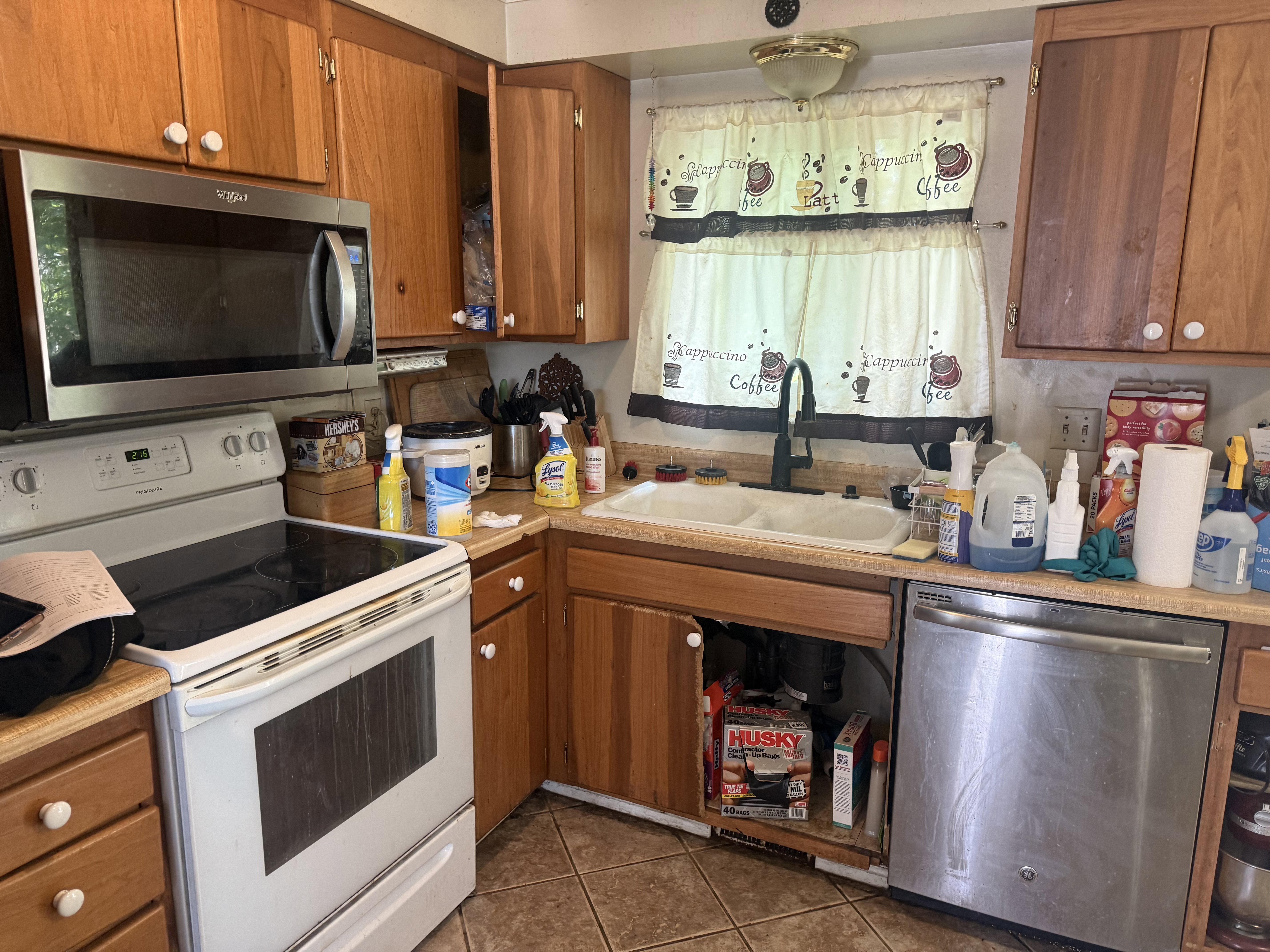 Kitchen featuring wood cabinetry, a double basin sink with a gooseneck faucet, a stainless steel over-the-range microwave, and a white electric range