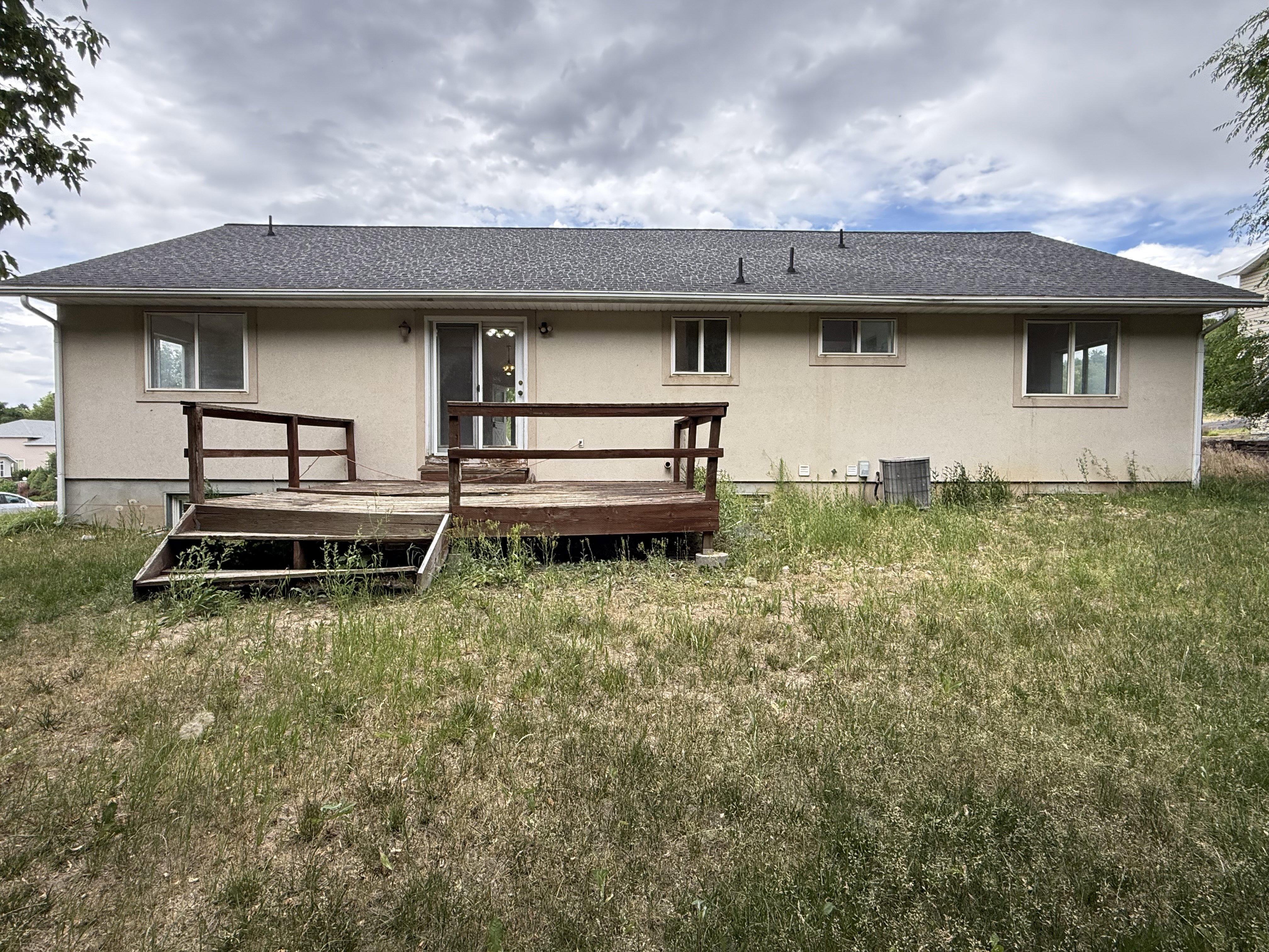 Rear exterior featuring a wood deck with railings, stucco siding, multiple windows, and a sliding glass door