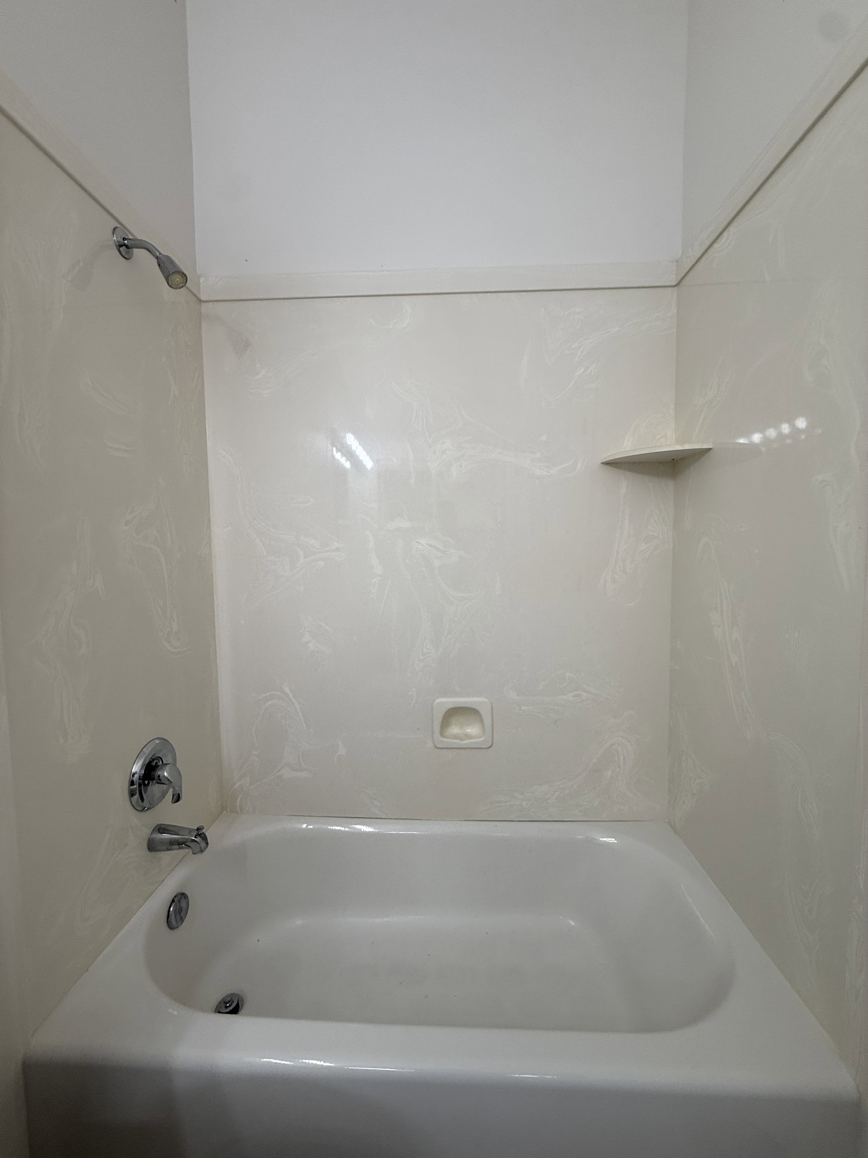White porcelain bathtub with chrome fixtures and light-toned, patterned wall surround