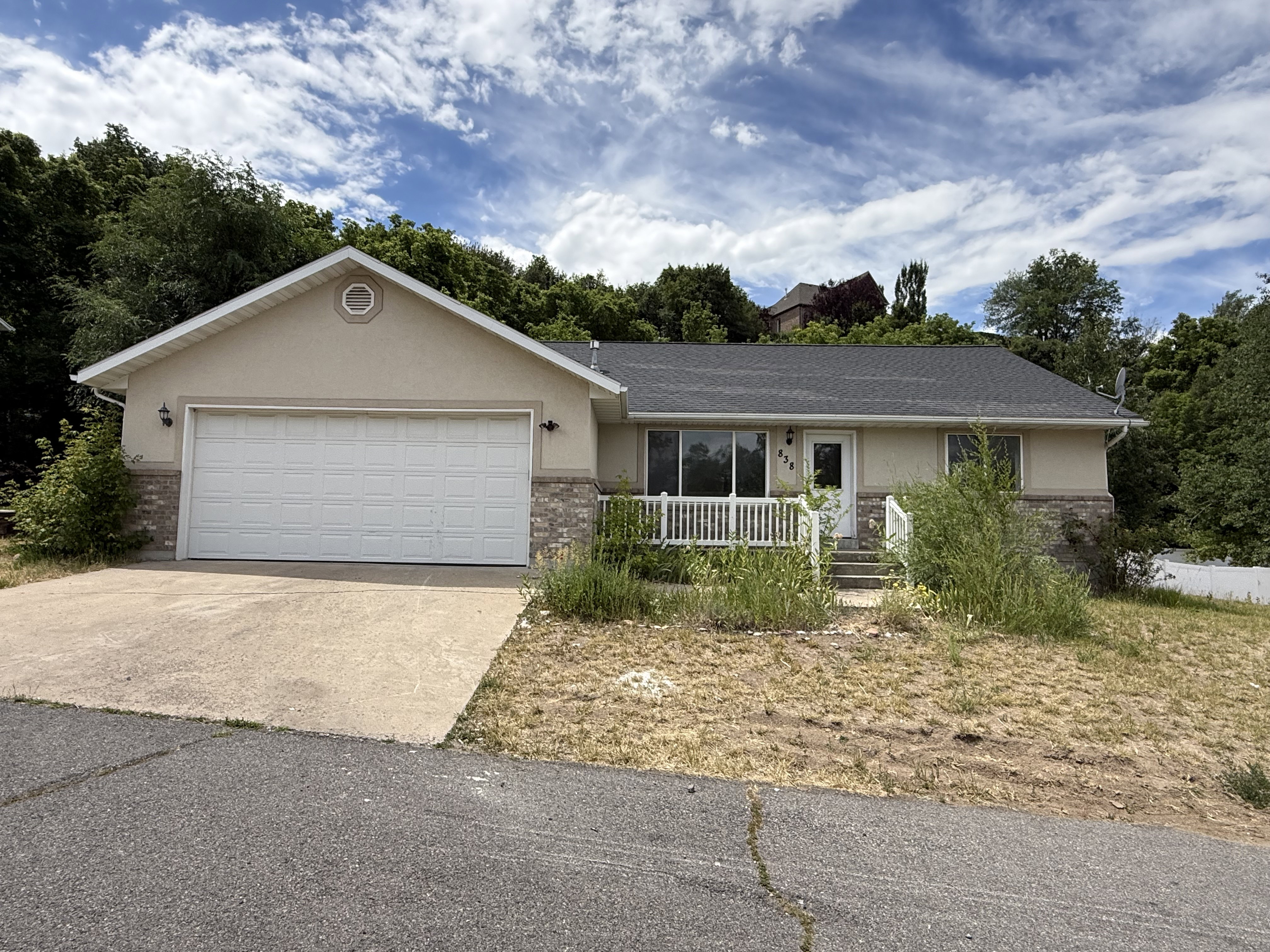 Ranch-style exterior featuring a stucco and stone facade, attached two-car garage, and front porch with white railing