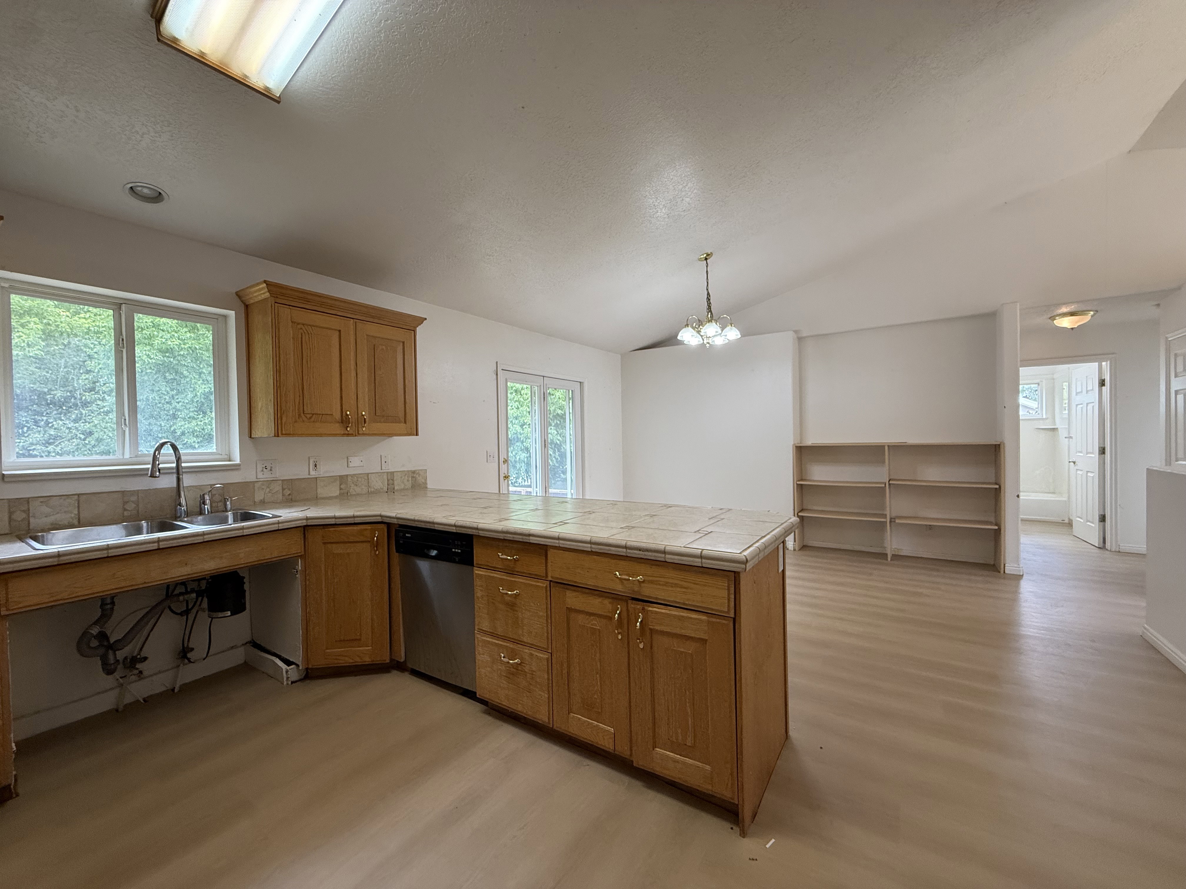 Kitchen featuring a central island with tiled countertop, wood cabinetry, dual basin stainless steel sink, and a stainless steel dishwasher