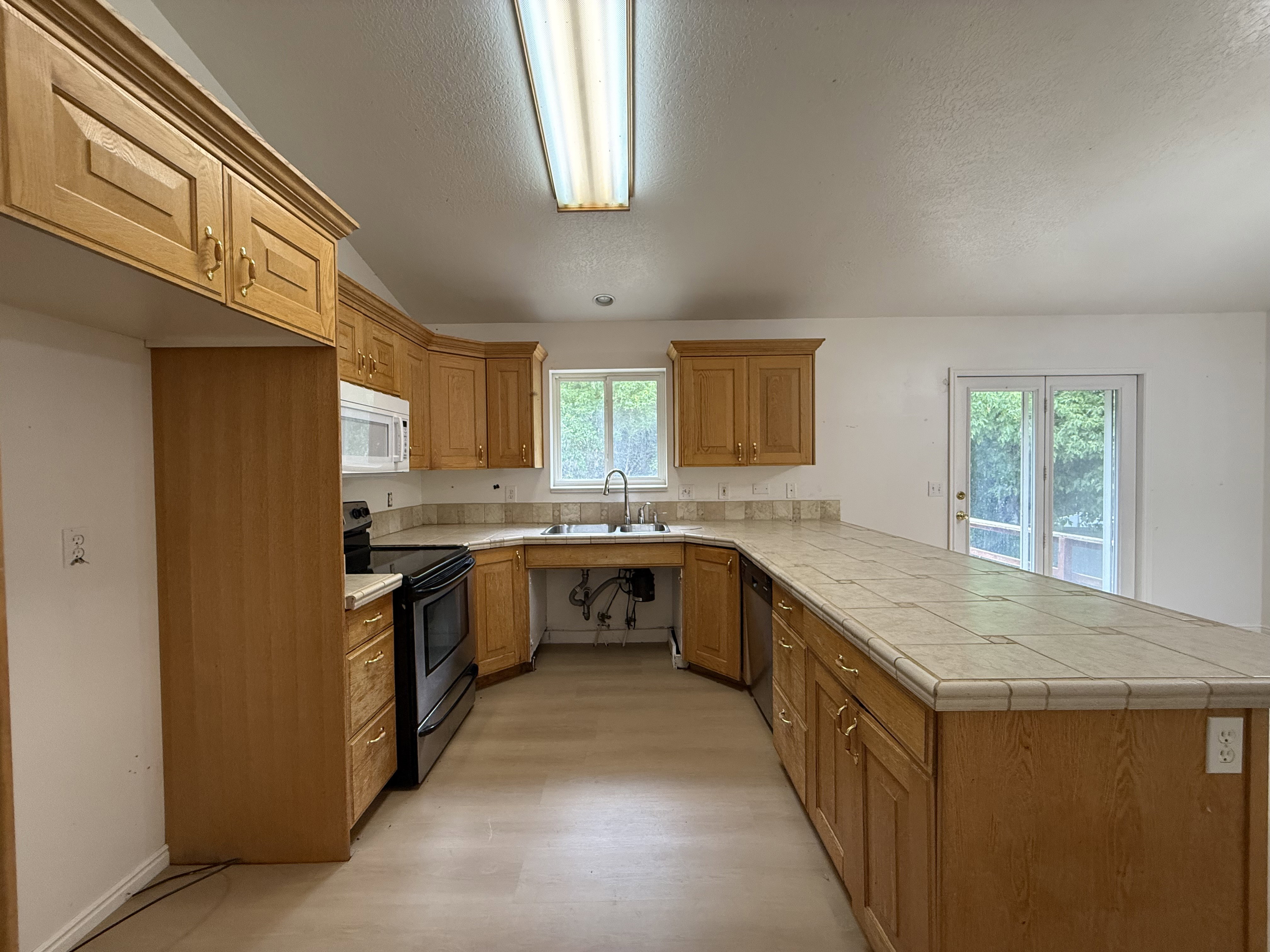 Kitchen featuring extensive wood cabinetry, tile countertops, a built-in microwave, an electric range, and wood-finish flooring