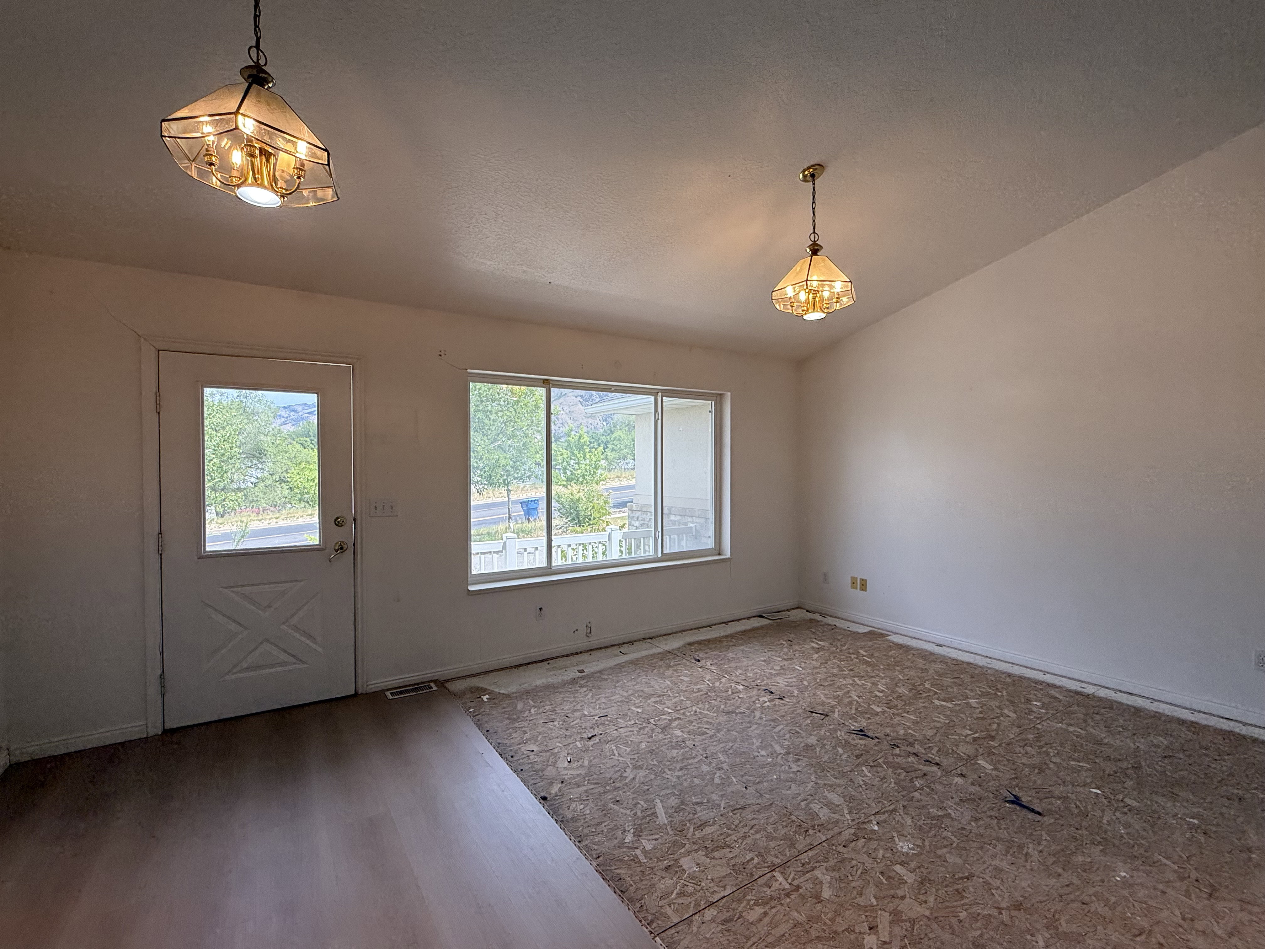 Vaulted ceiling room with partial wood-finish flooring and two pendant light fixtures