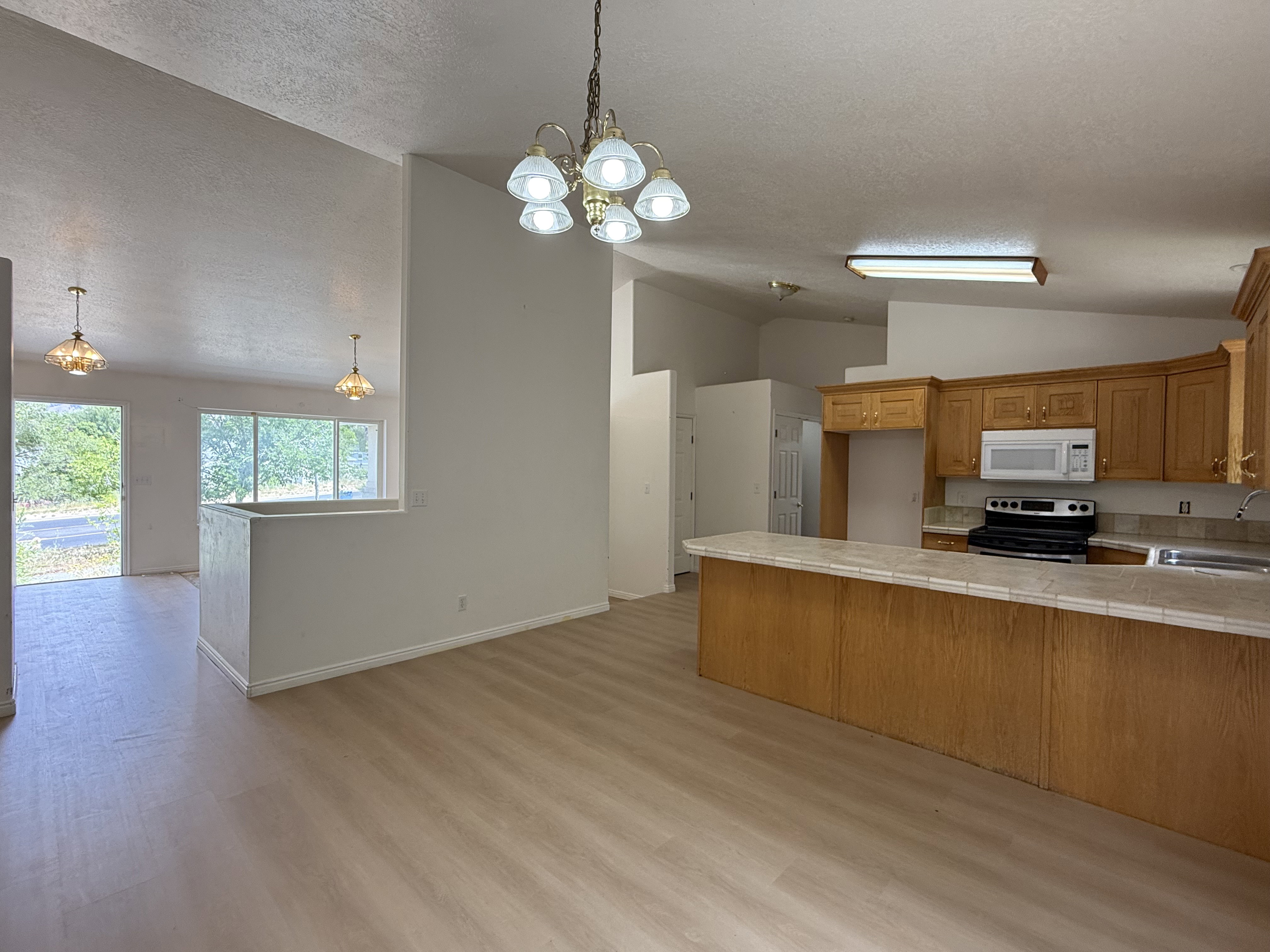 Open-concept kitchen and living area featuring wood-finish flooring, vaulted ceilings, and a kitchen island with a tiled countertop