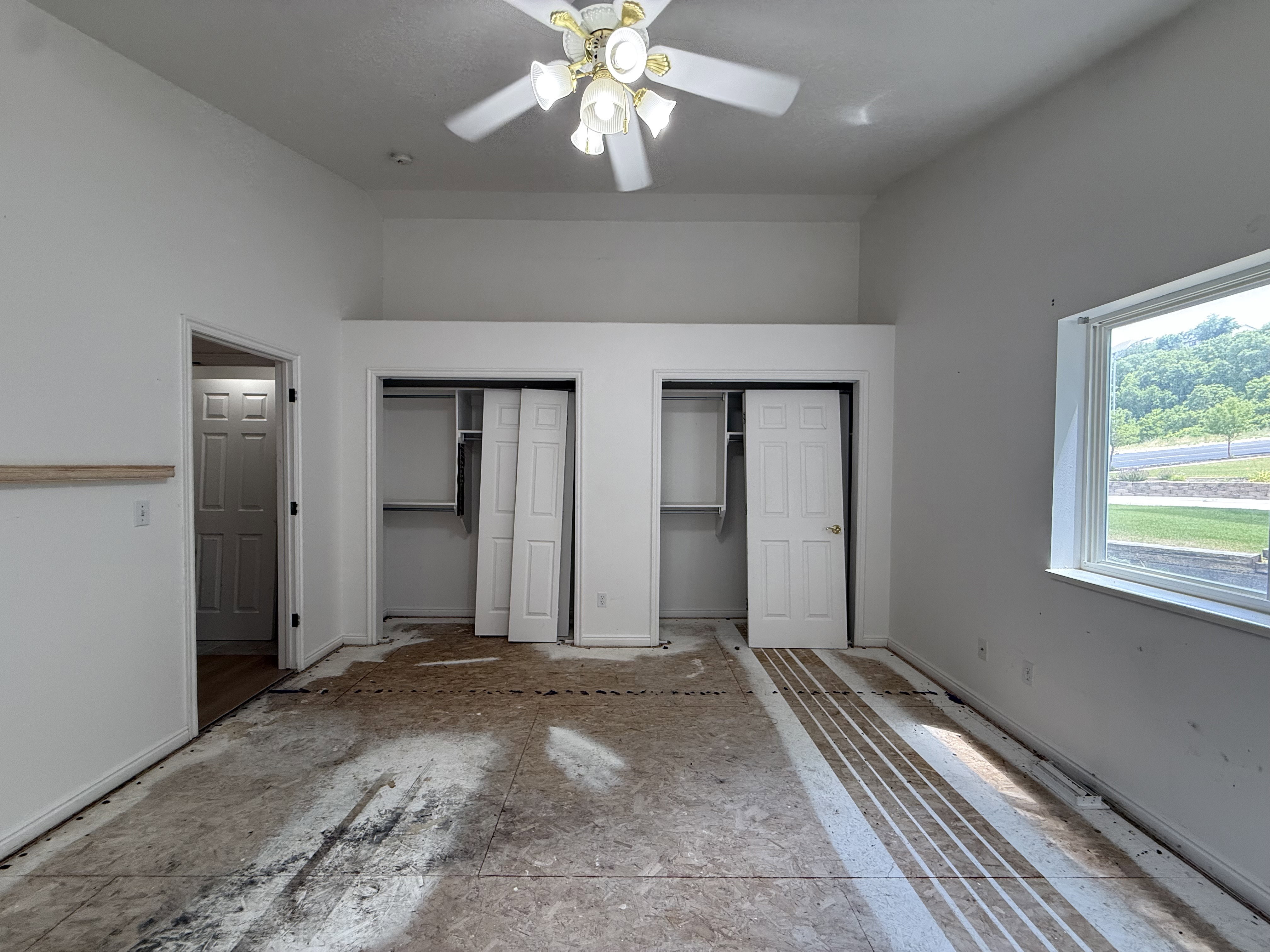 Spacious room featuring vaulted ceilings, a ceiling fan, dual closet spaces with bi-fold doors, and a large window providing ample natural light