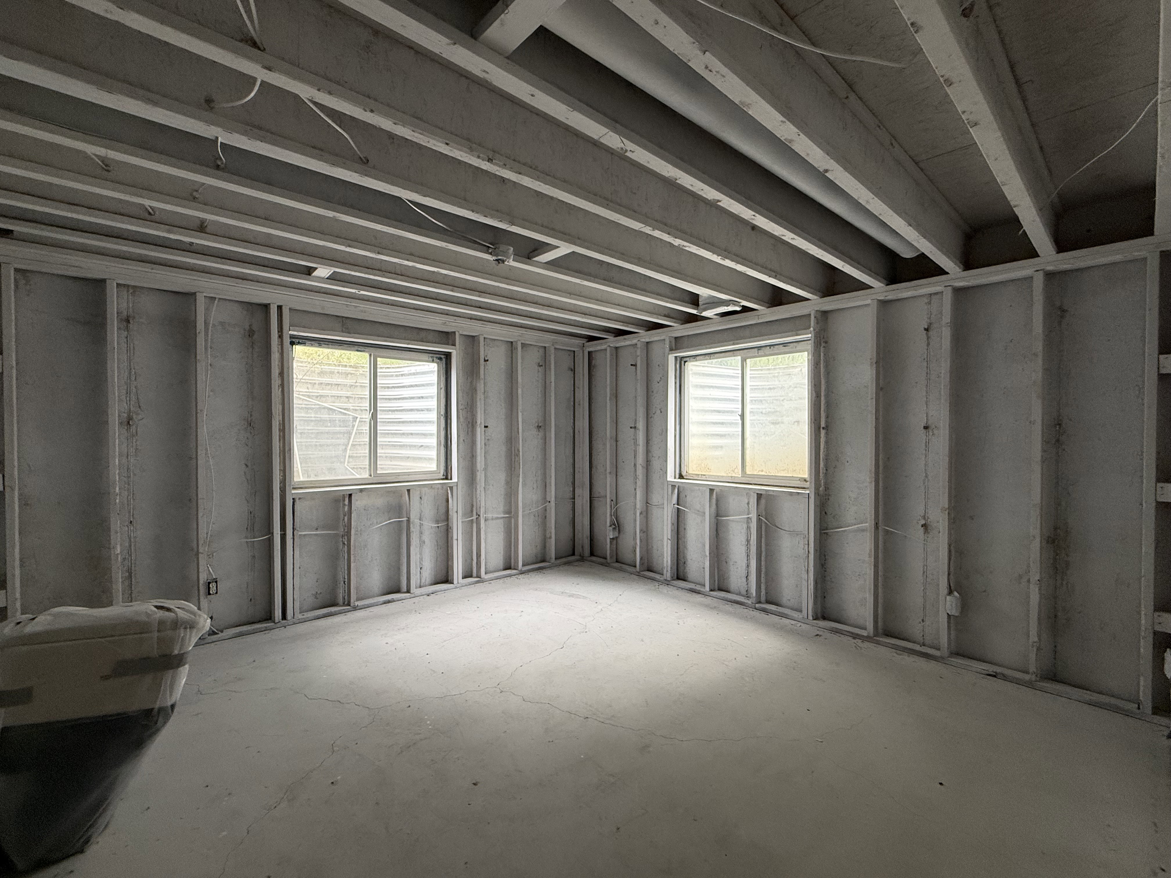 Unfinished basement space featuring exposed ceiling joists, framed walls, and two egress windows
