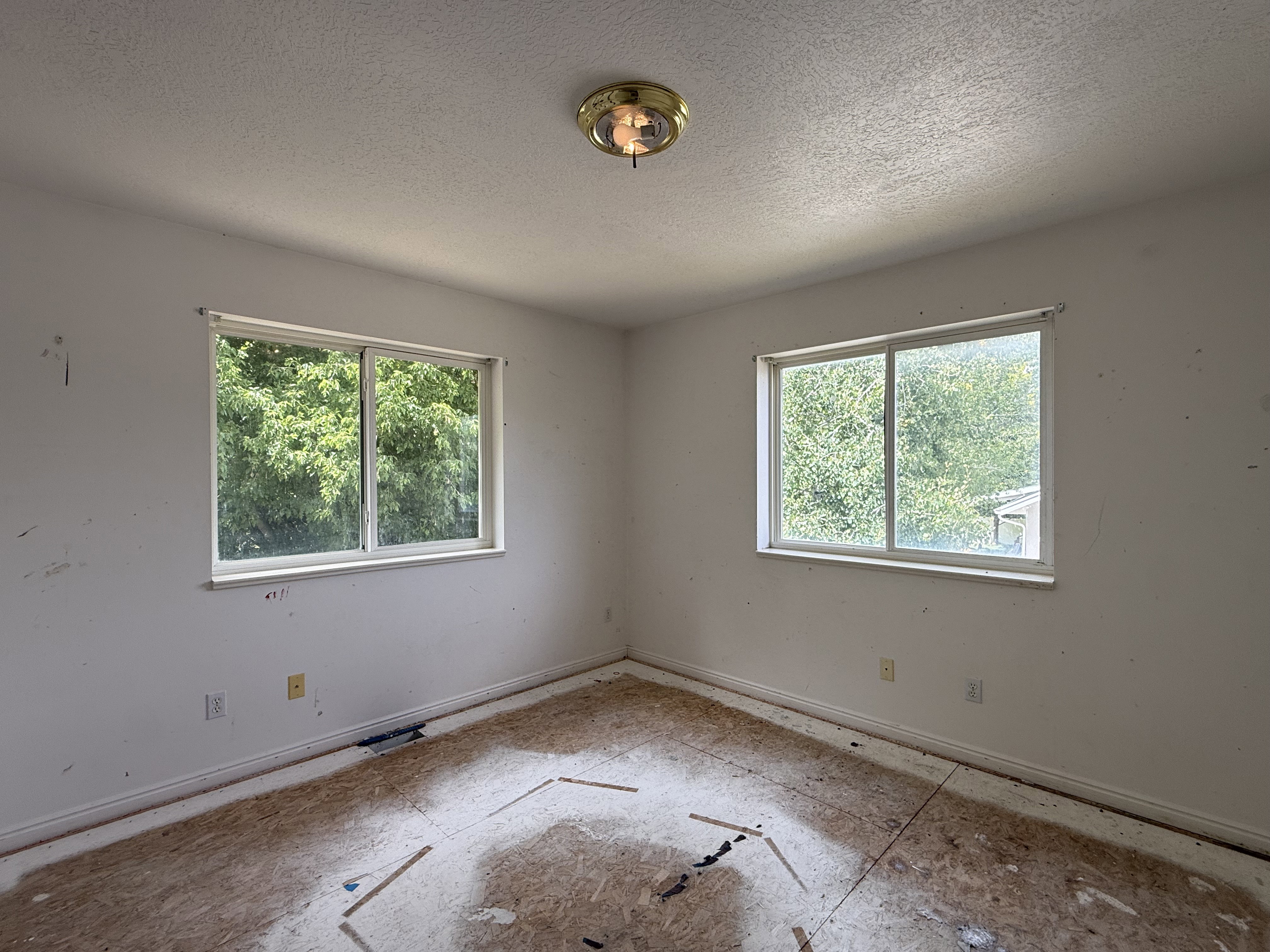 Room featuring two large windows with white trim, a semi-flush mount ceiling light fixture, and raw subflooring