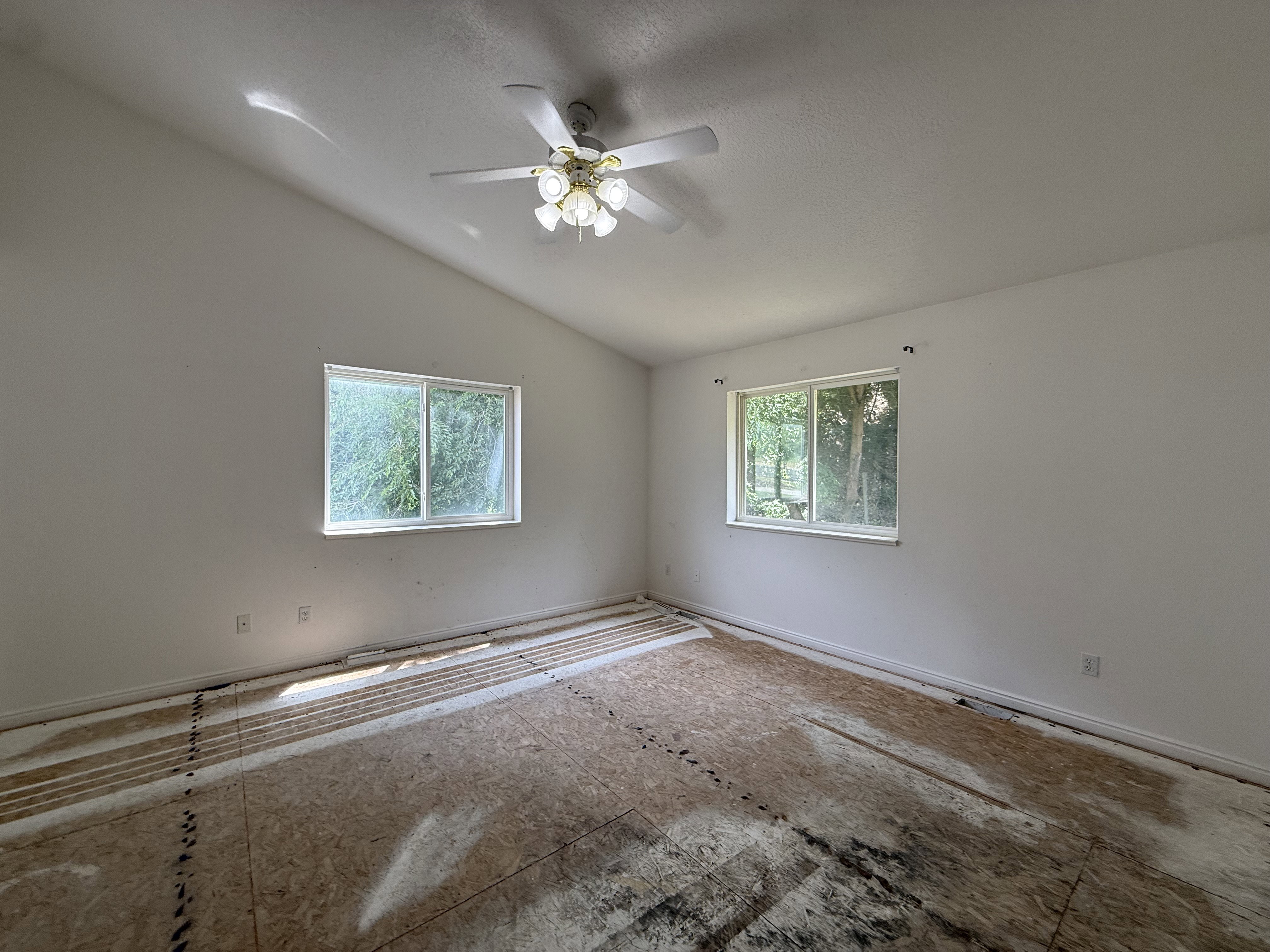 Room with vaulted ceiling, two windows, and exposed subflooring
