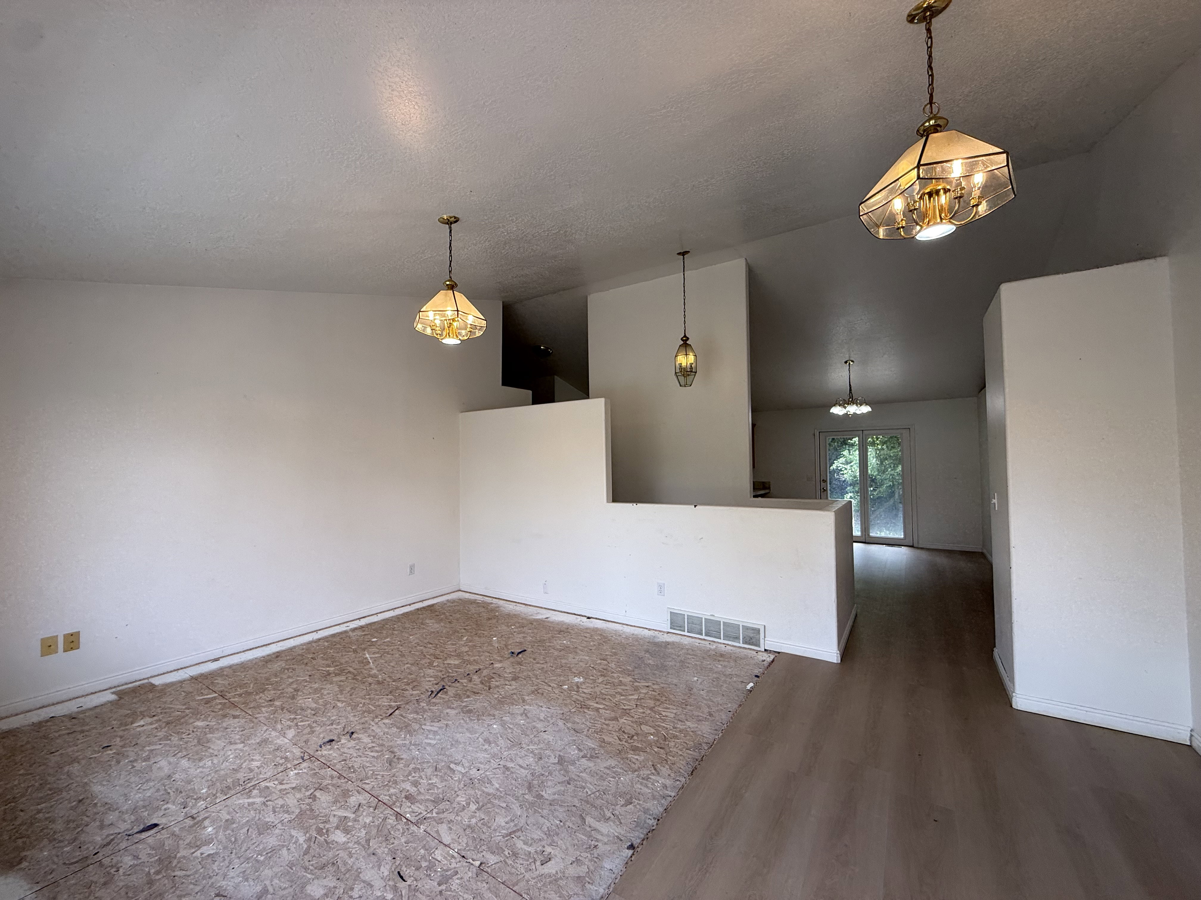 Expansive interior space featuring a partial wall, multiple pendant light fixtures, and a combination of subfloor and wood-finish flooring