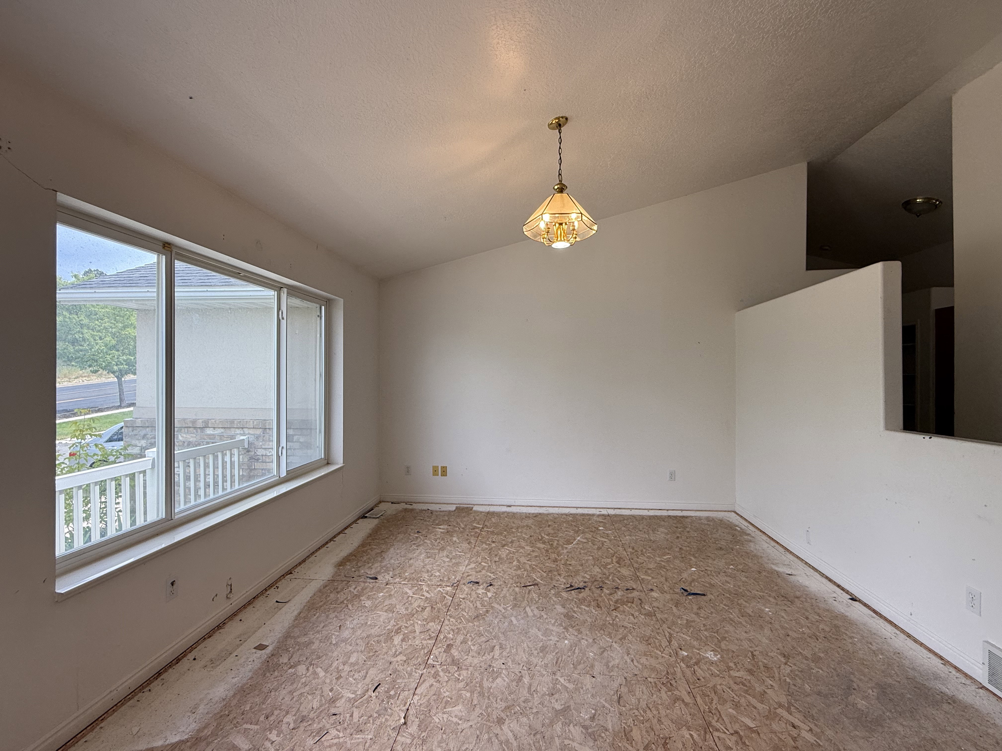 Interior room with unfinished subfloor, a large window, vaulted ceiling, and a hanging pendant light fixture