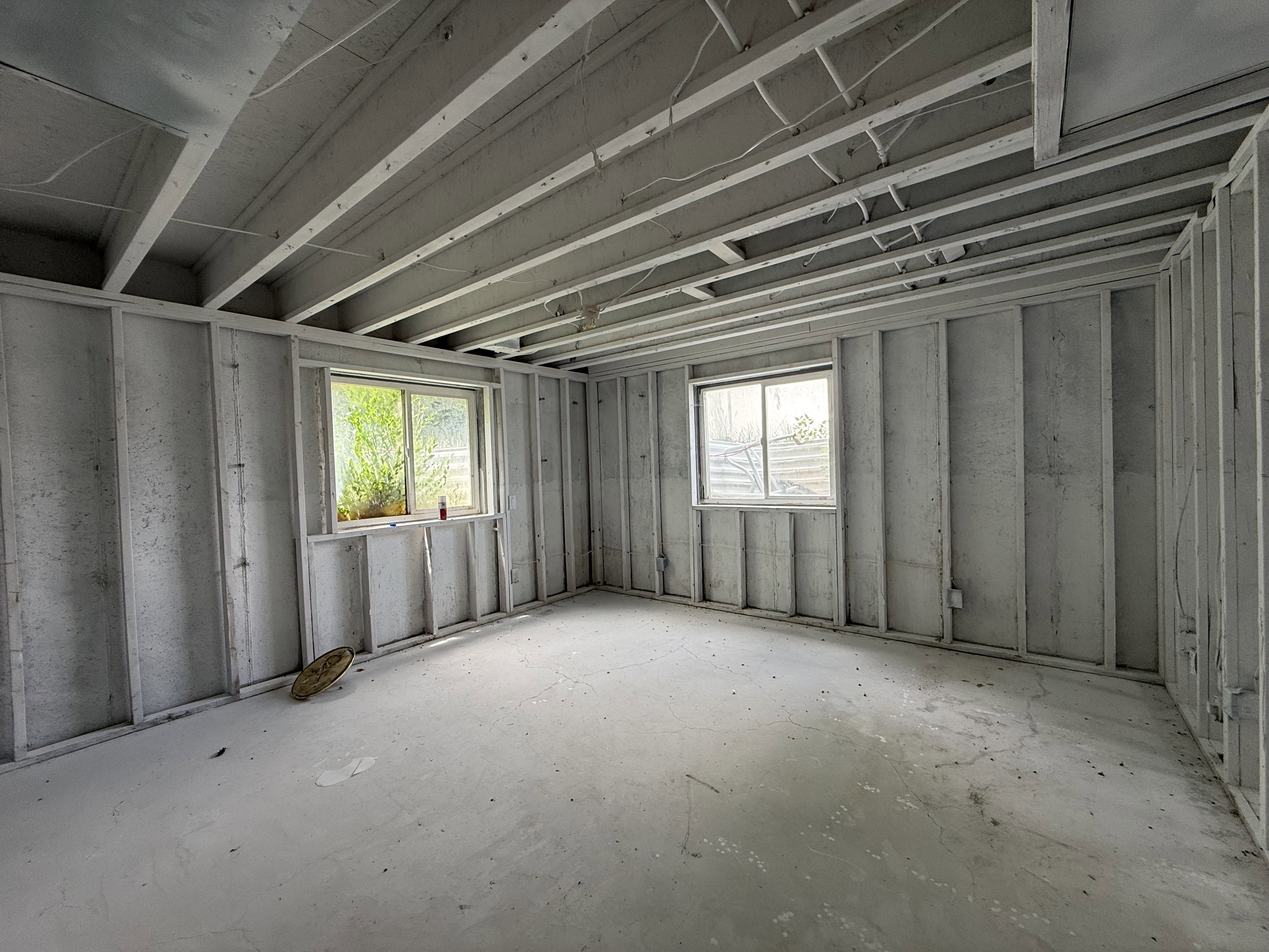 Unfinished room featuring exposed ceiling joists and framed walls, two windows with white trim, and a concrete floor
