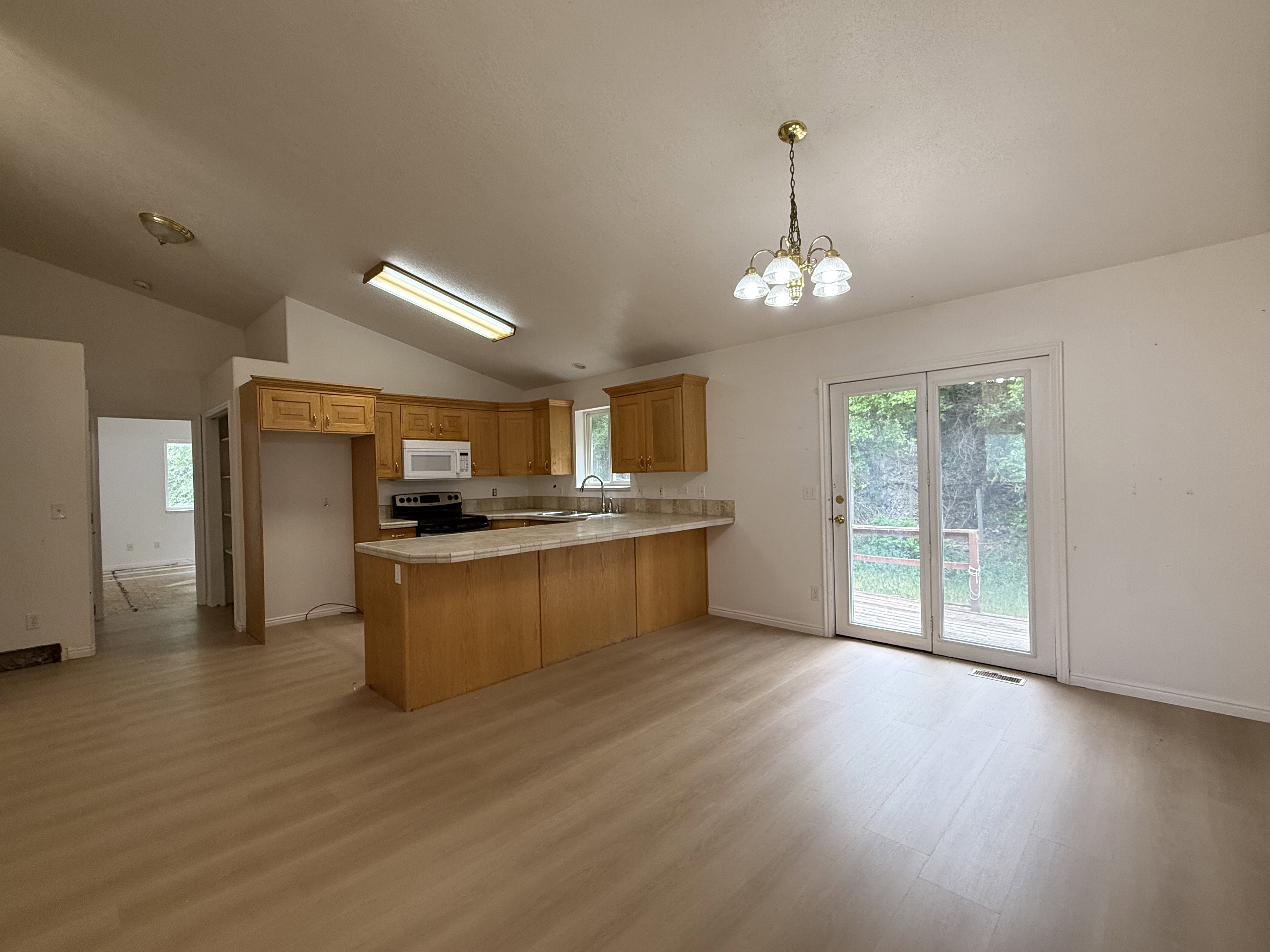 Open-concept kitchen and dining area featuring wood-finish flooring, vaulted ceilings, and a light wood cabinetry kitchen with a built-in microwave