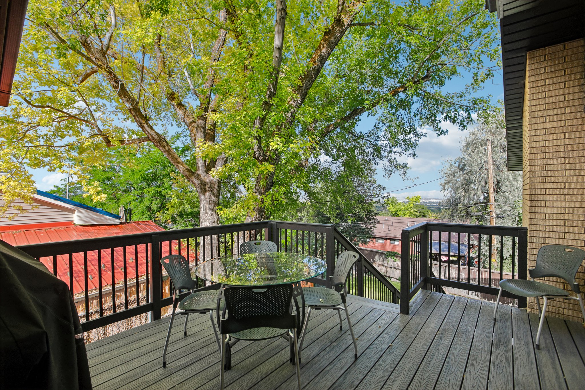 Expansive outdoor deck featuring composite decking, dark wood railing, and mature trees providing natural shade