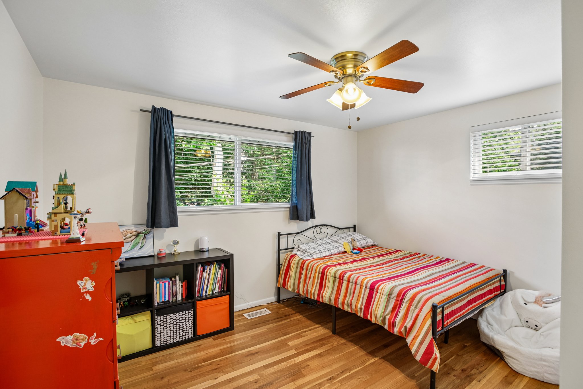 Room featuring wood-finish flooring, two windows with blinds, and a ceiling fan with integrated lighting