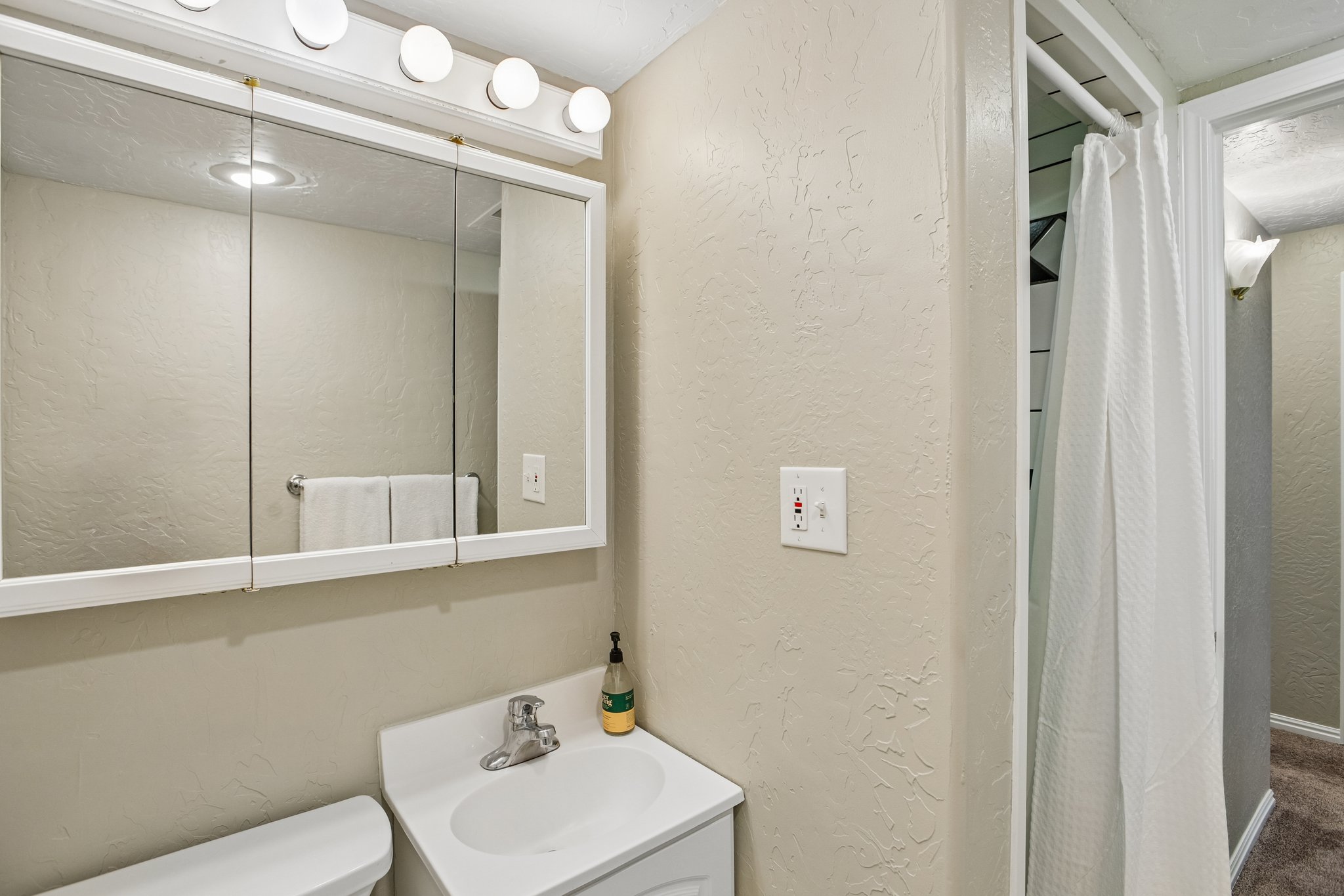 Bathroom vanity with a tri-fold mirrored medicine cabinet, a four-bulb light fixture, and an integrated sink