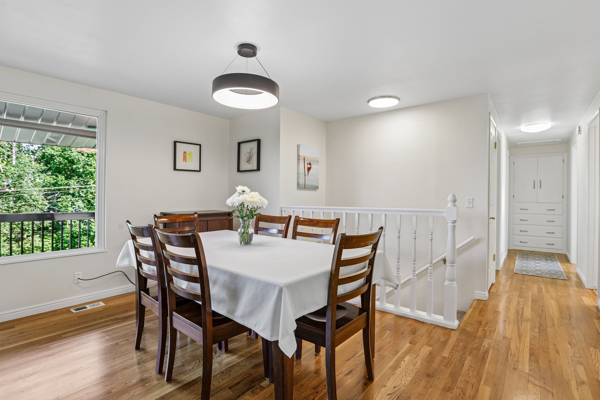 Hardwood flooring throughout, featuring a modern ring pendant light fixture, a window with a black railing, and a white painted banister