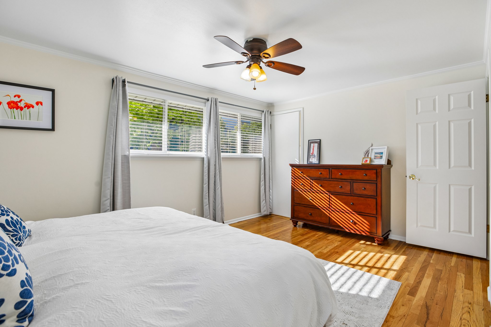 Bedroom featuring wood-finish flooring, two large windows with blinds, a ceiling fan with integrated lighting, and crown molding