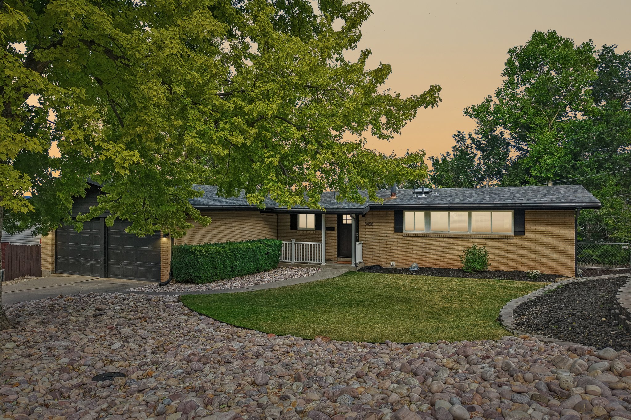 Brick exterior featuring a two-car garage, established trees, and a manicured lawn