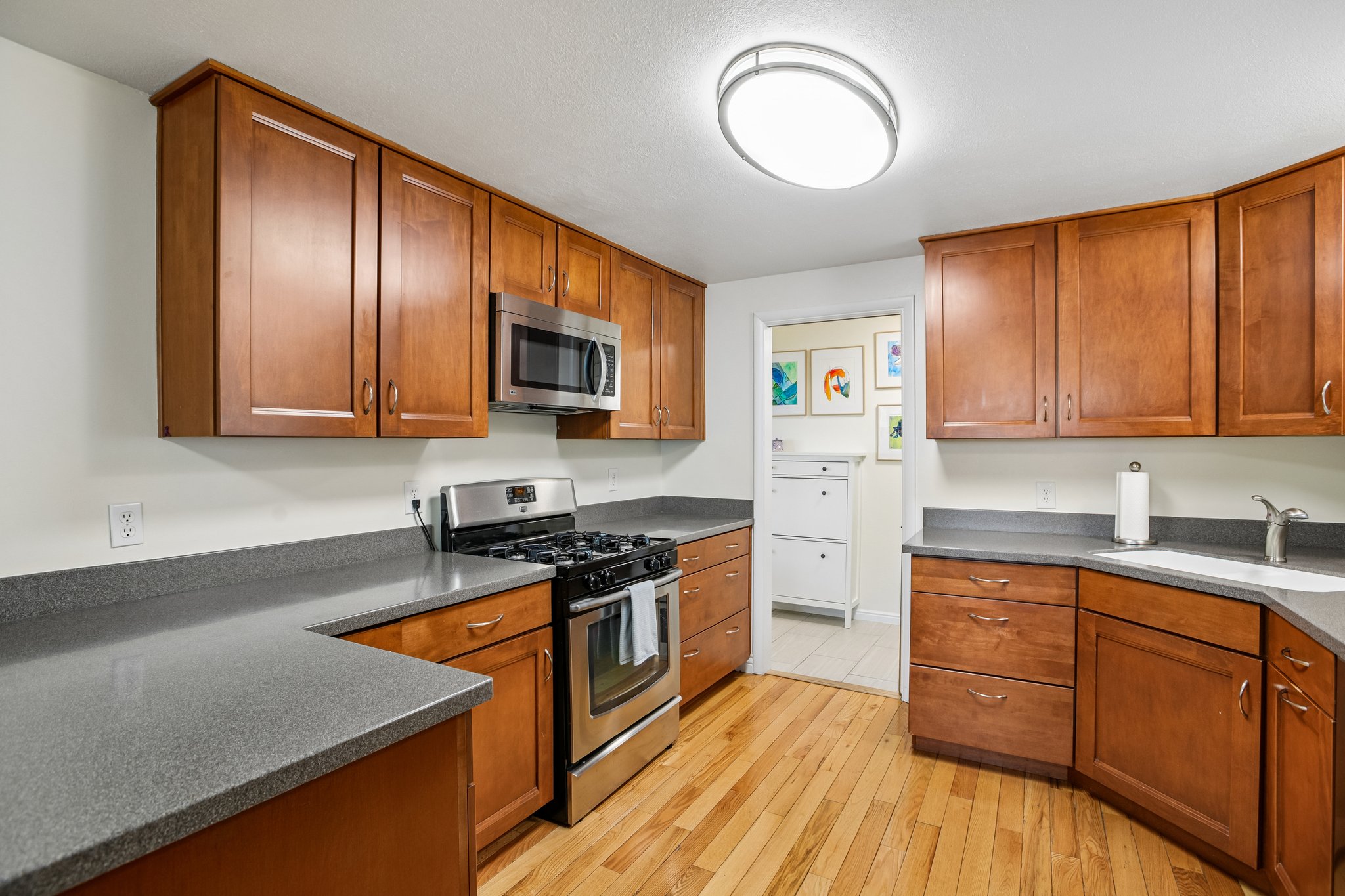U-shaped kitchen featuring wood-finish cabinetry, dark countertops, hardwood flooring, and stainless steel appliances