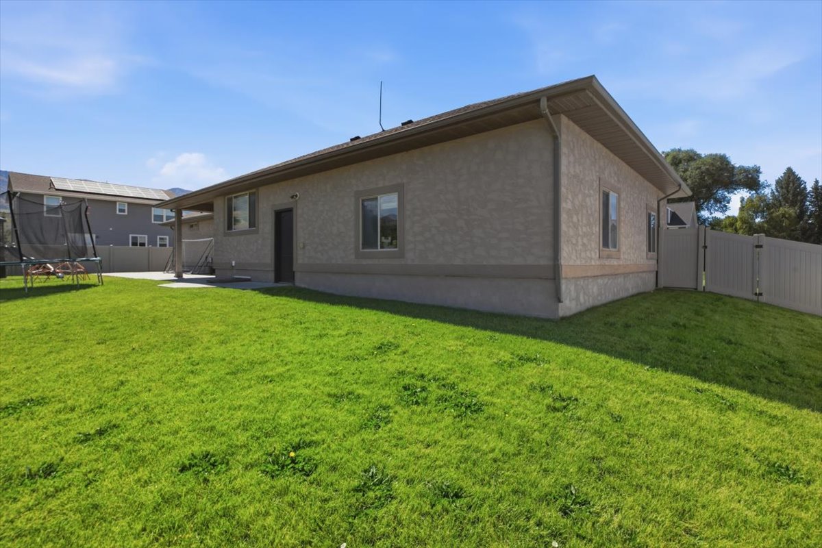 Spacious backyard featuring a stucco exterior, a covered patio, a concrete pad, a private fence, and a vibrant green lawn