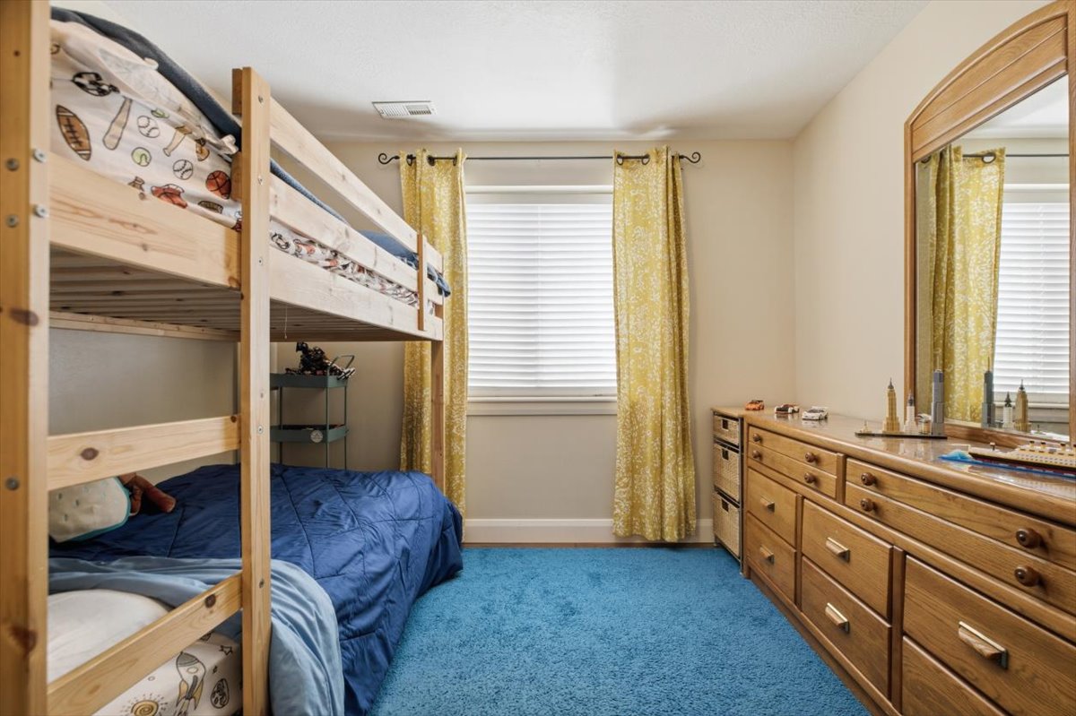 Bedroom featuring a window with blinds and gold curtains, a built-in wooden dresser with mirror, and blue carpet flooring